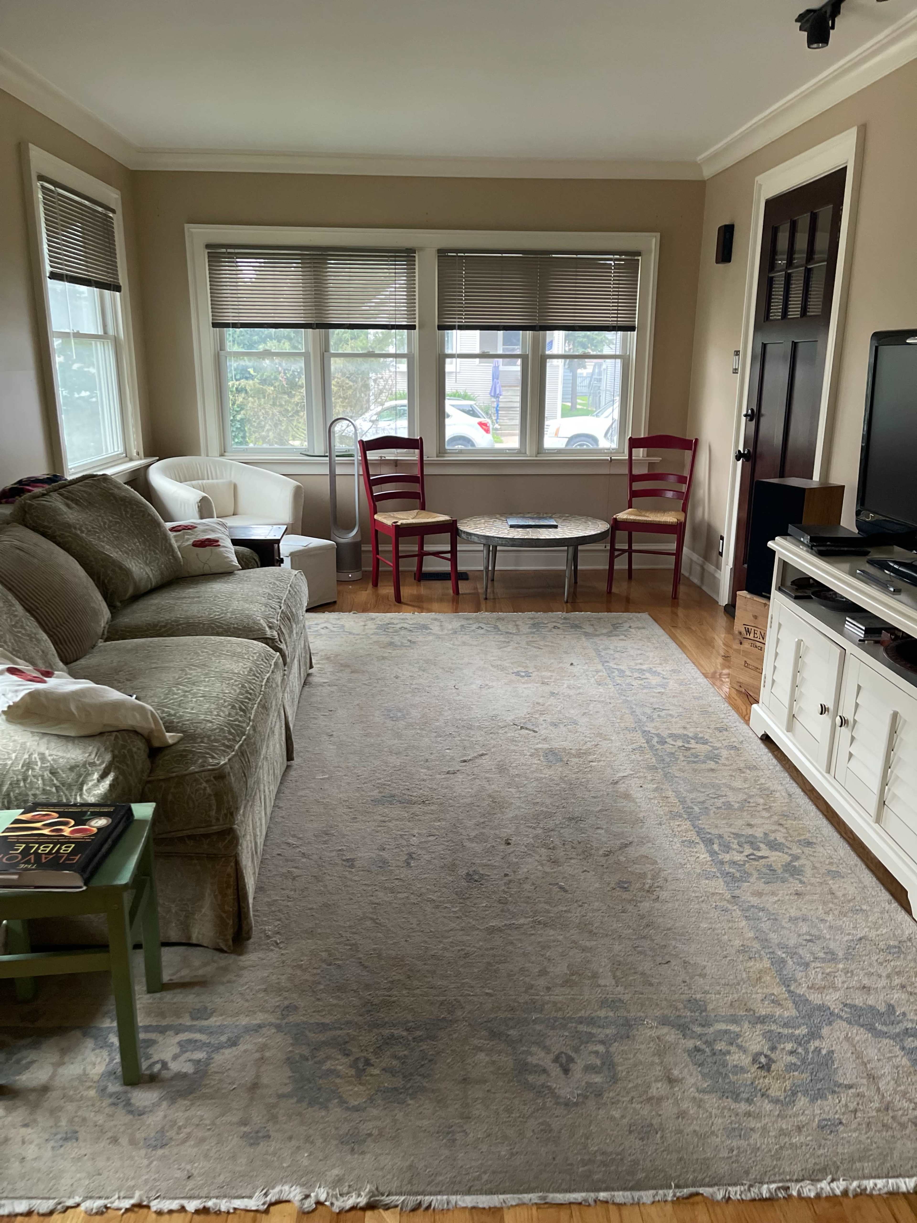 The image depicts a cozy living room with a sofa, two red chairs, a coffee table, and a light-colored rug on a wooden floor.