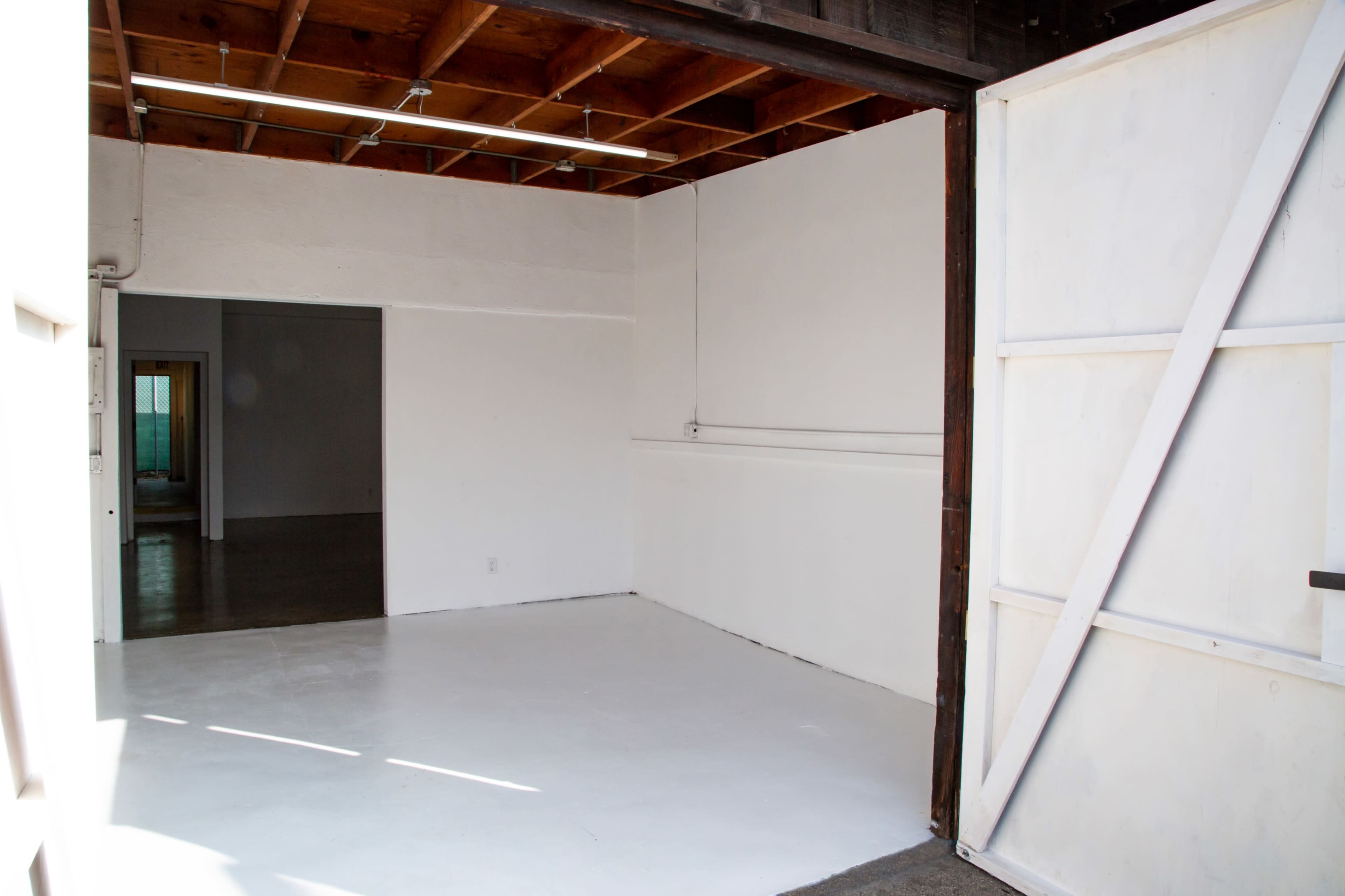 An empty room with white walls and a concrete floor, featuring an open door leading to another room.
