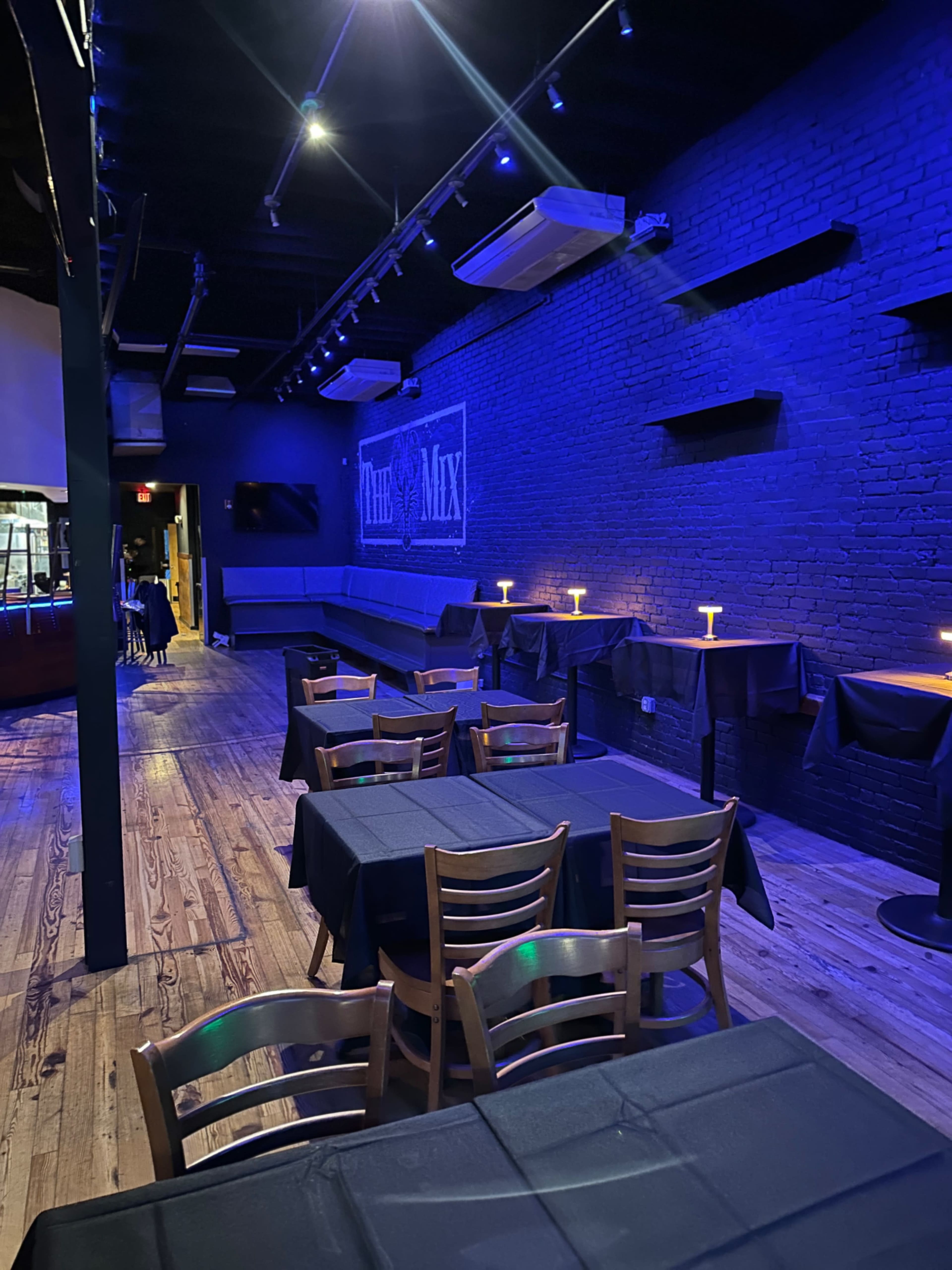 A dimly lit restaurant or bar with blue lighting, featuring several tables covered in black cloth and a wall displaying the word "Mix."