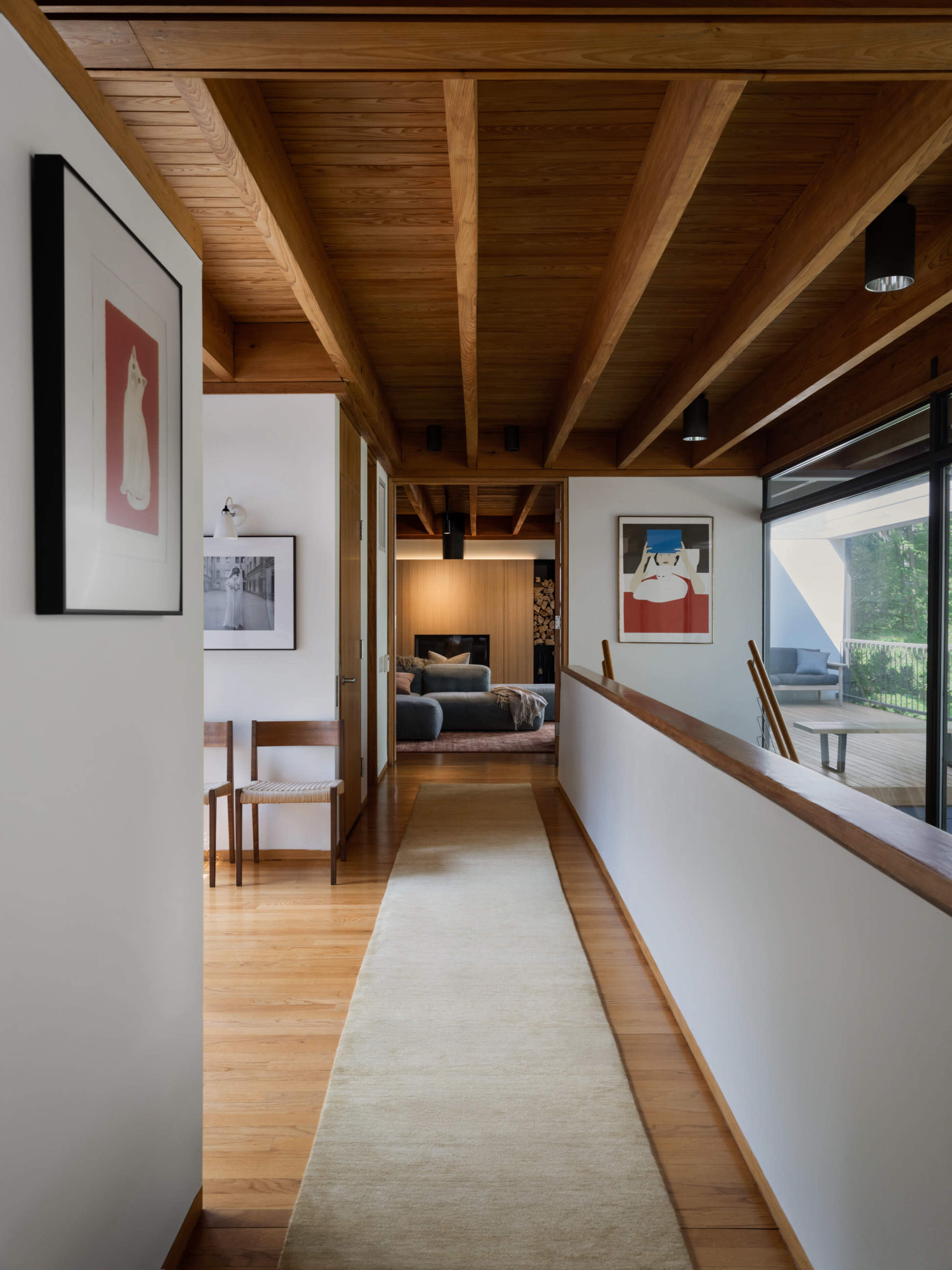 A wooden-paneled hallway features framed artwork on the walls, leading to an open living space with large windows.