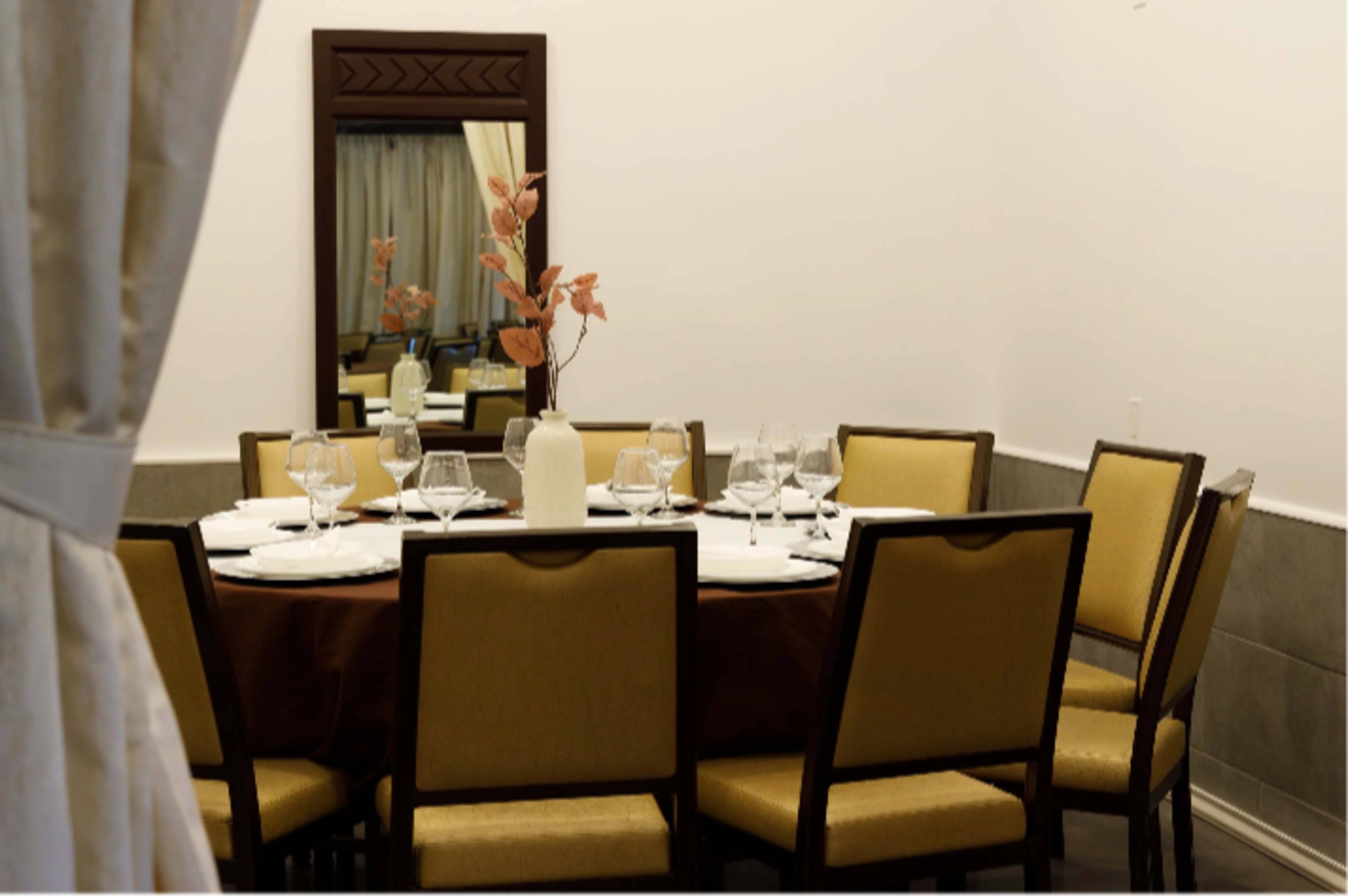 A round dining table is set with glassware and a vase of flowers in a well-decorated room featuring a mirror and elegant seating.