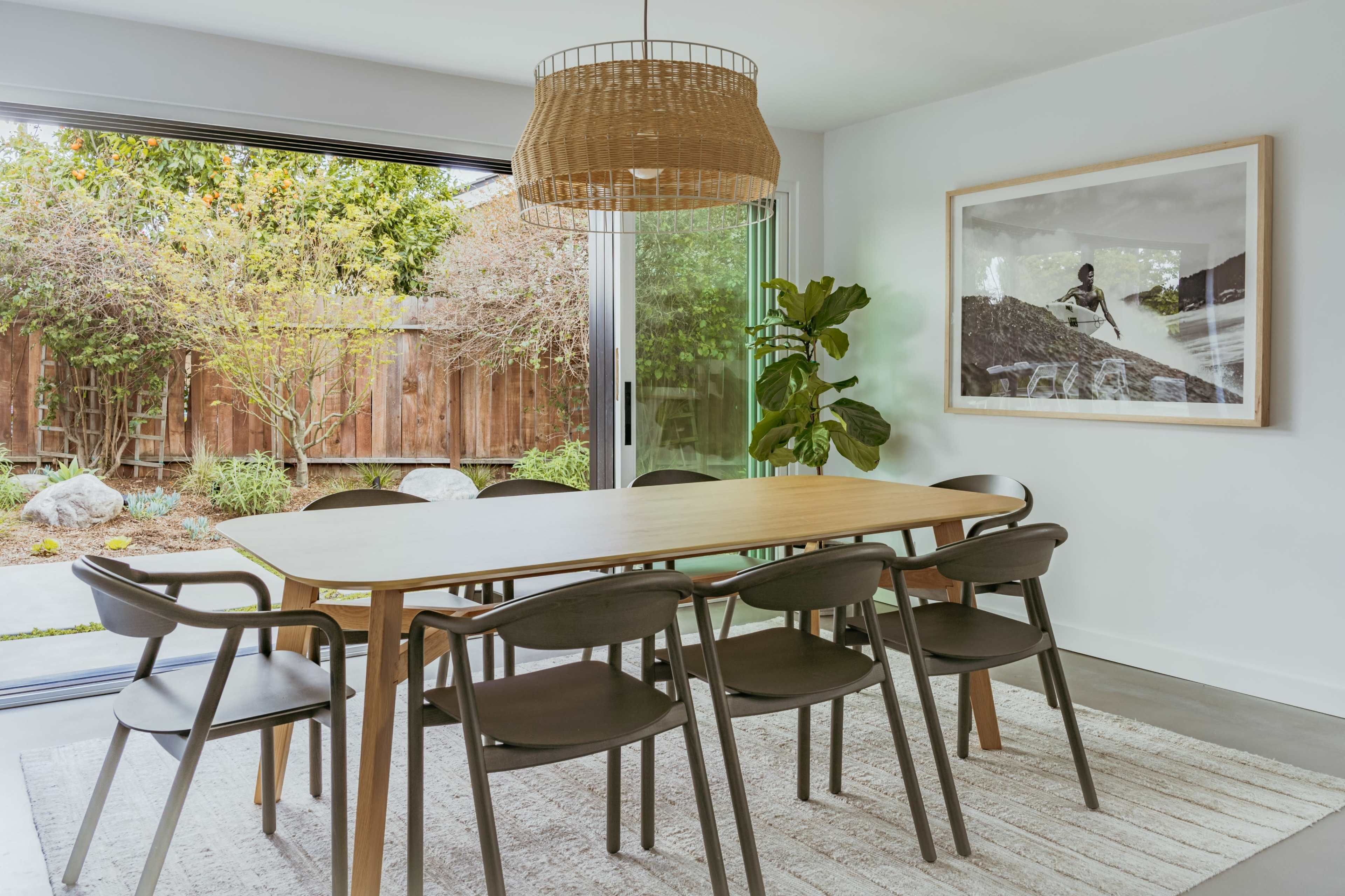 A dining area features a wooden table surrounded by chairs, with large glass doors opening to a garden outside.