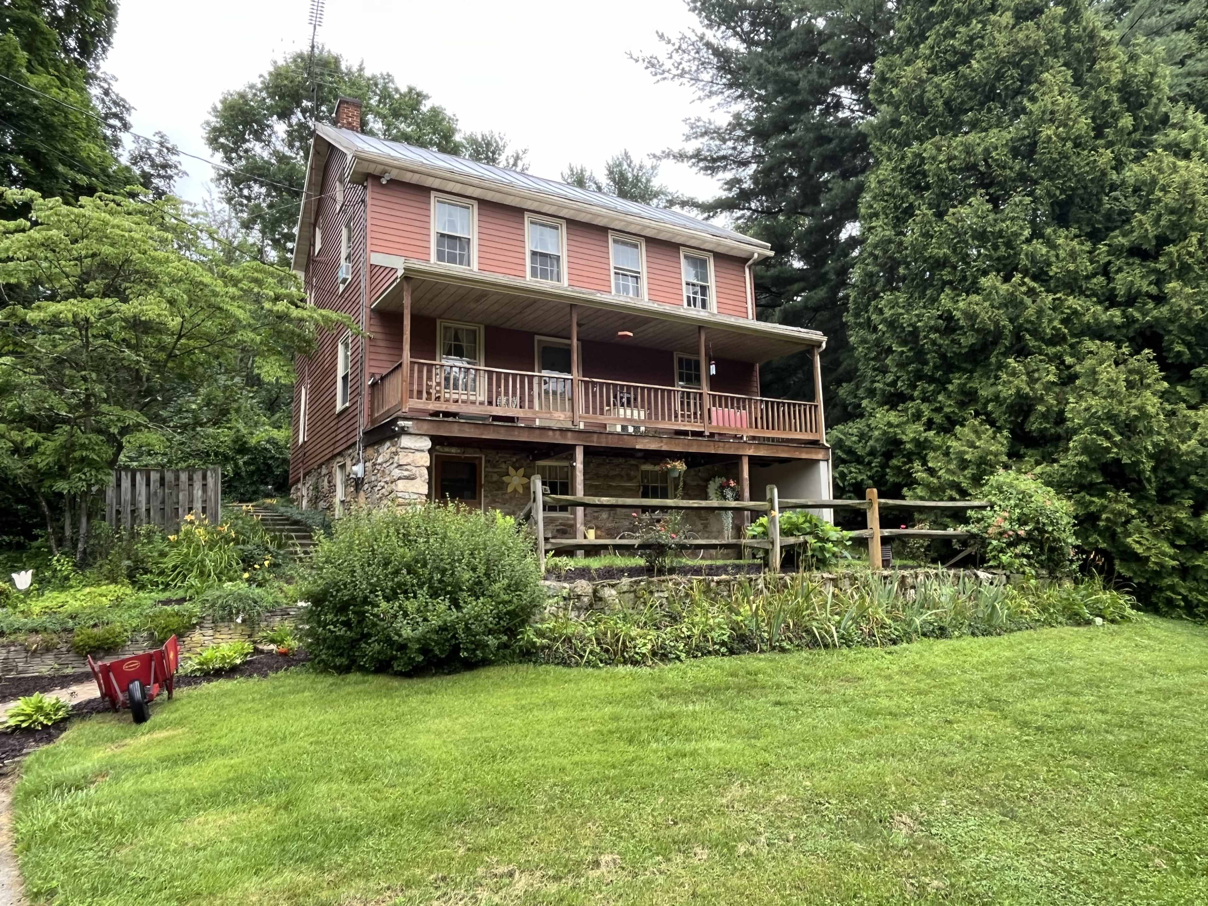 A three-story house with a red exterior and a front porch is surrounded by greenery and a well-maintained garden.