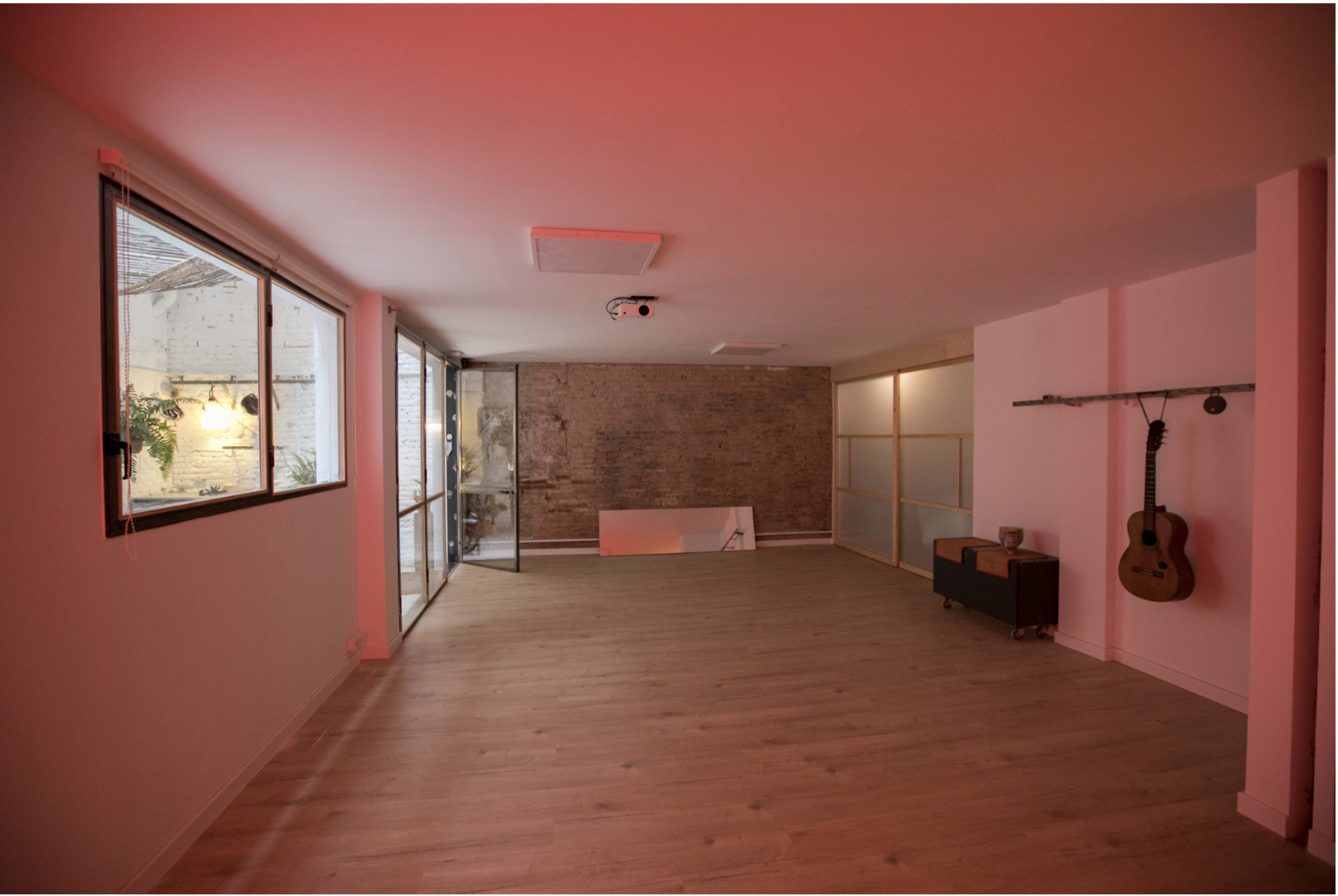 An empty room with wooden flooring, a brick wall, large windows, and a guitar hanging on the wall.