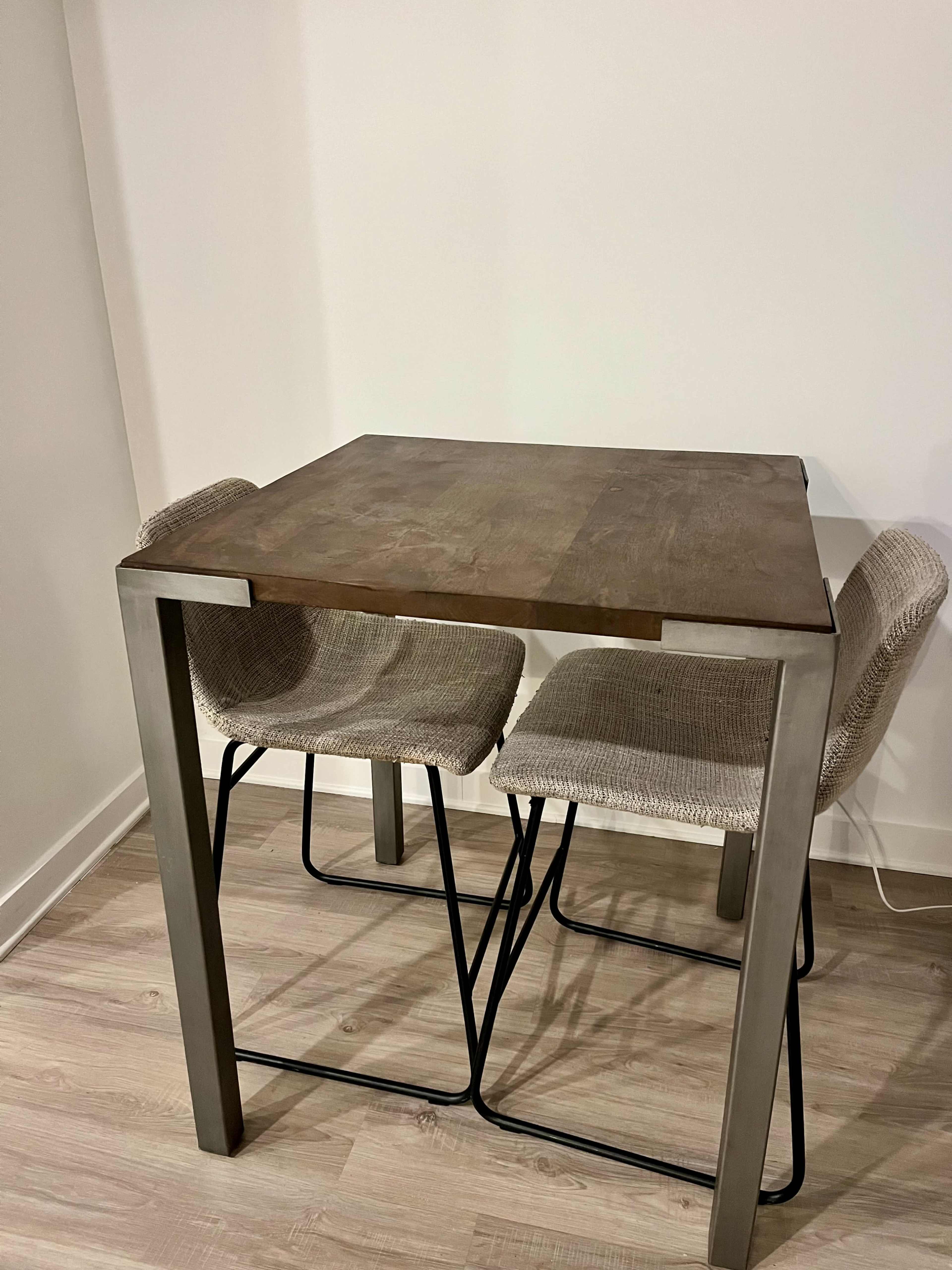 A wooden table with a metal frame sits between two woven chairs on a light-colored floor.