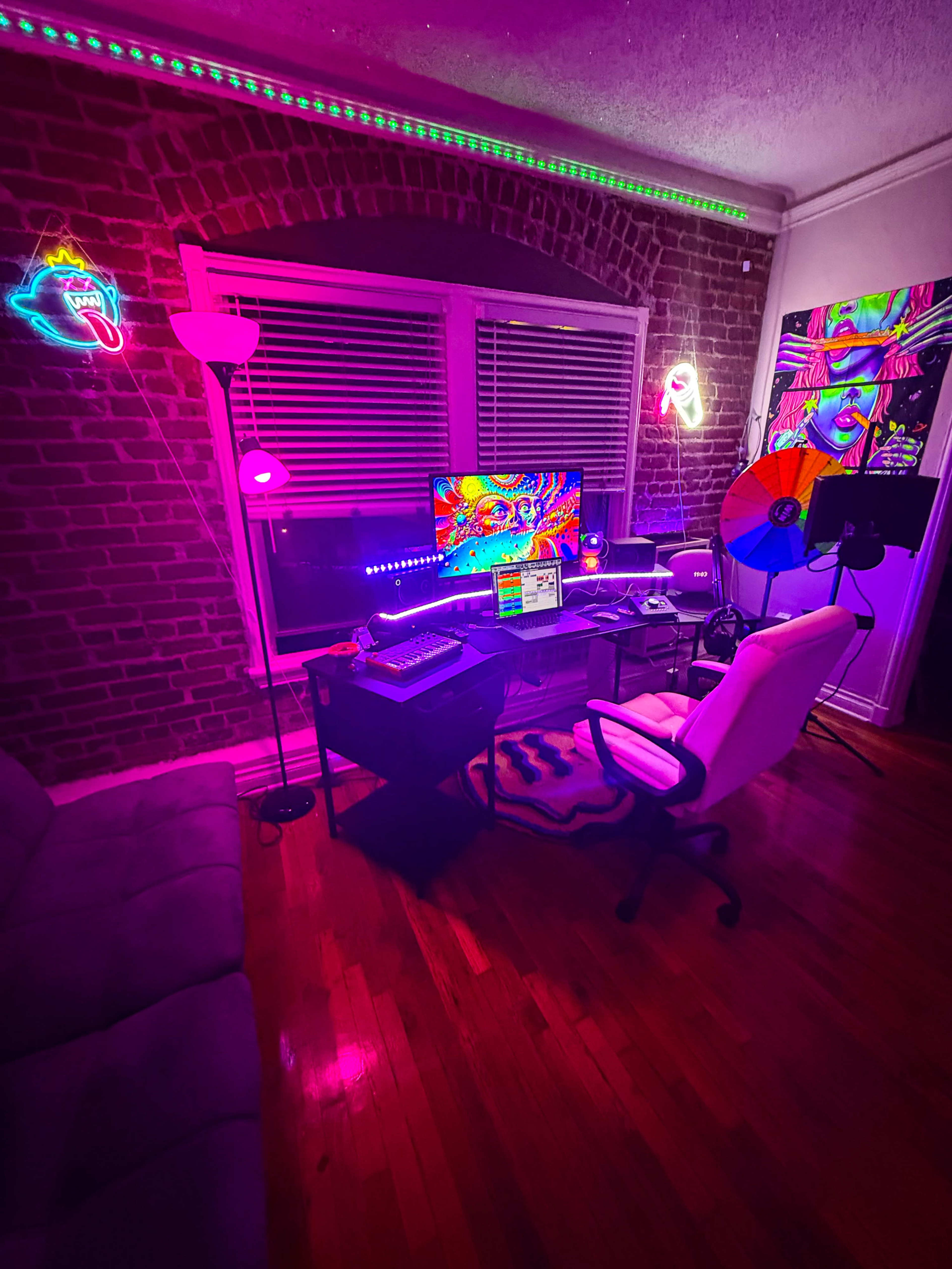 The image depicts a vibrant, colorful workspace featuring a computer desk with a monitor, surrounded by neon lights and a brick wall backdrop.