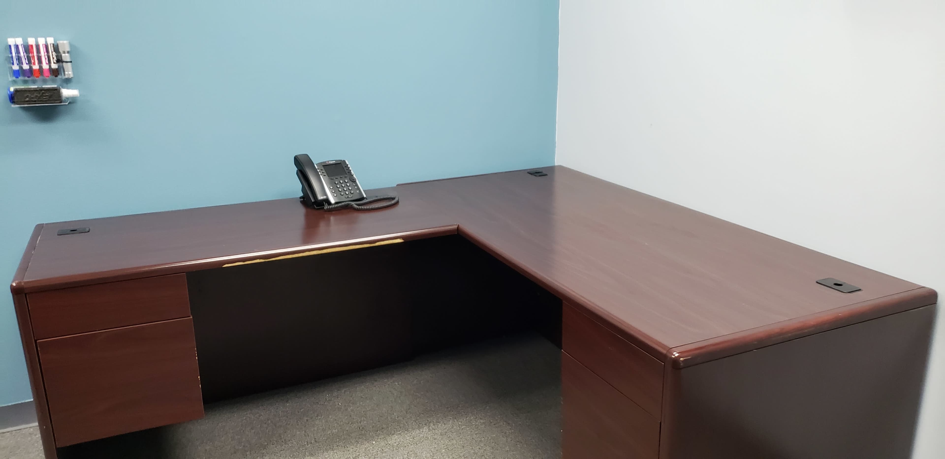 An empty office desk with a telephone on it, positioned against a blue wall.