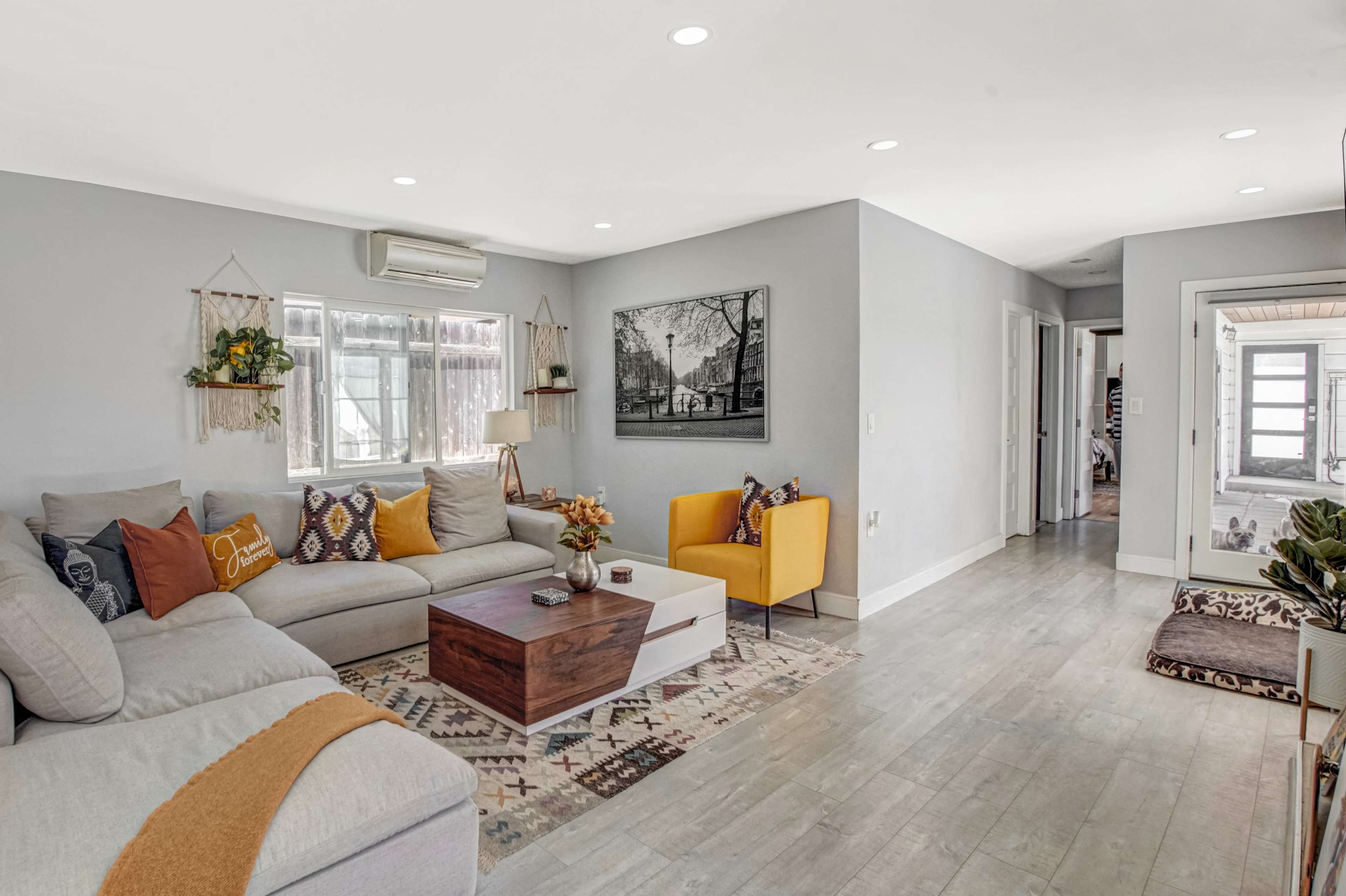 A bright, modern living room features a sectional sofa, a coffee table, and two accent chairs, with natural light streaming through the windows.