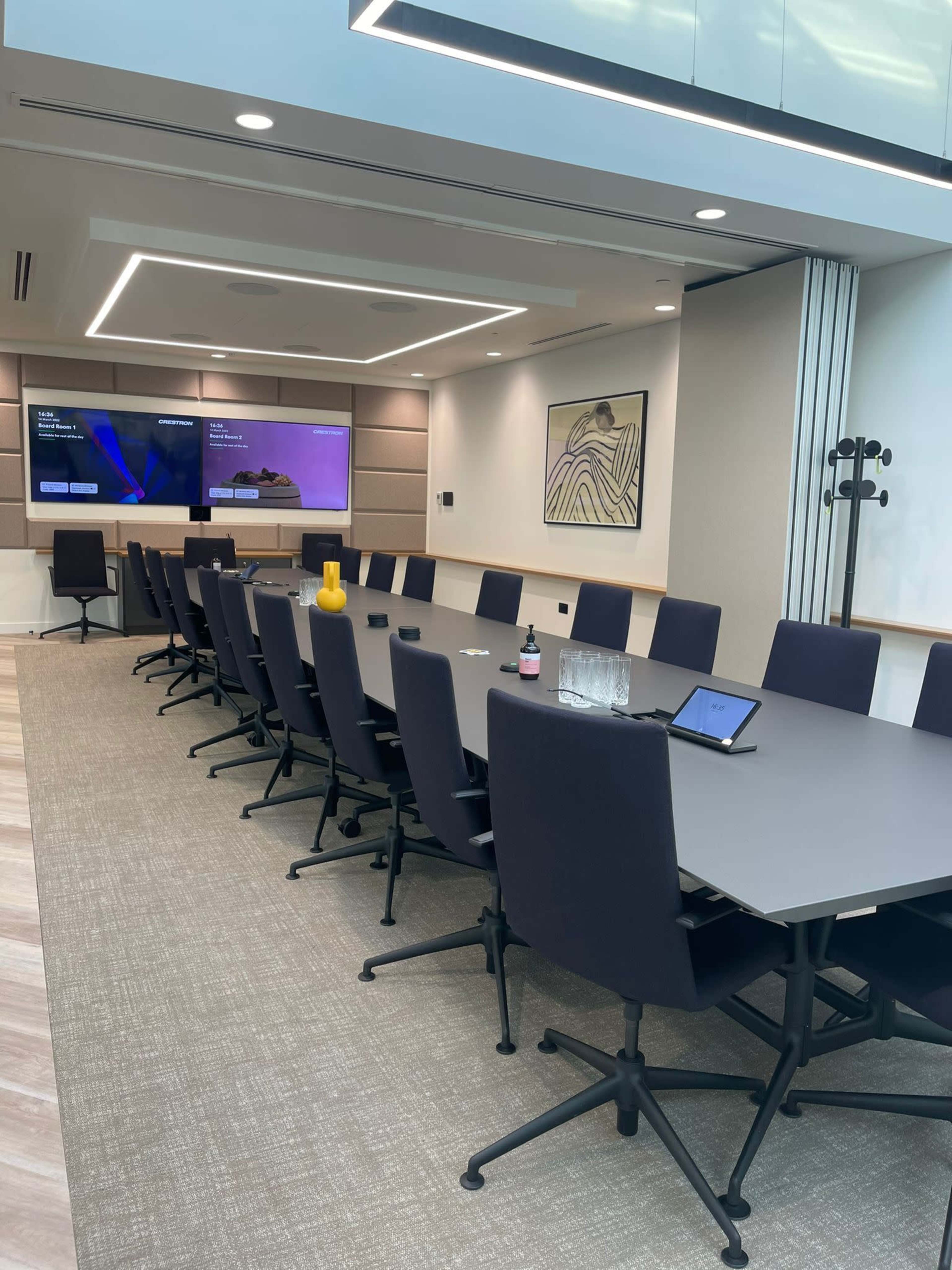 A modern conference room with a long table, black chairs, a large screen, and minimal decorative elements.
