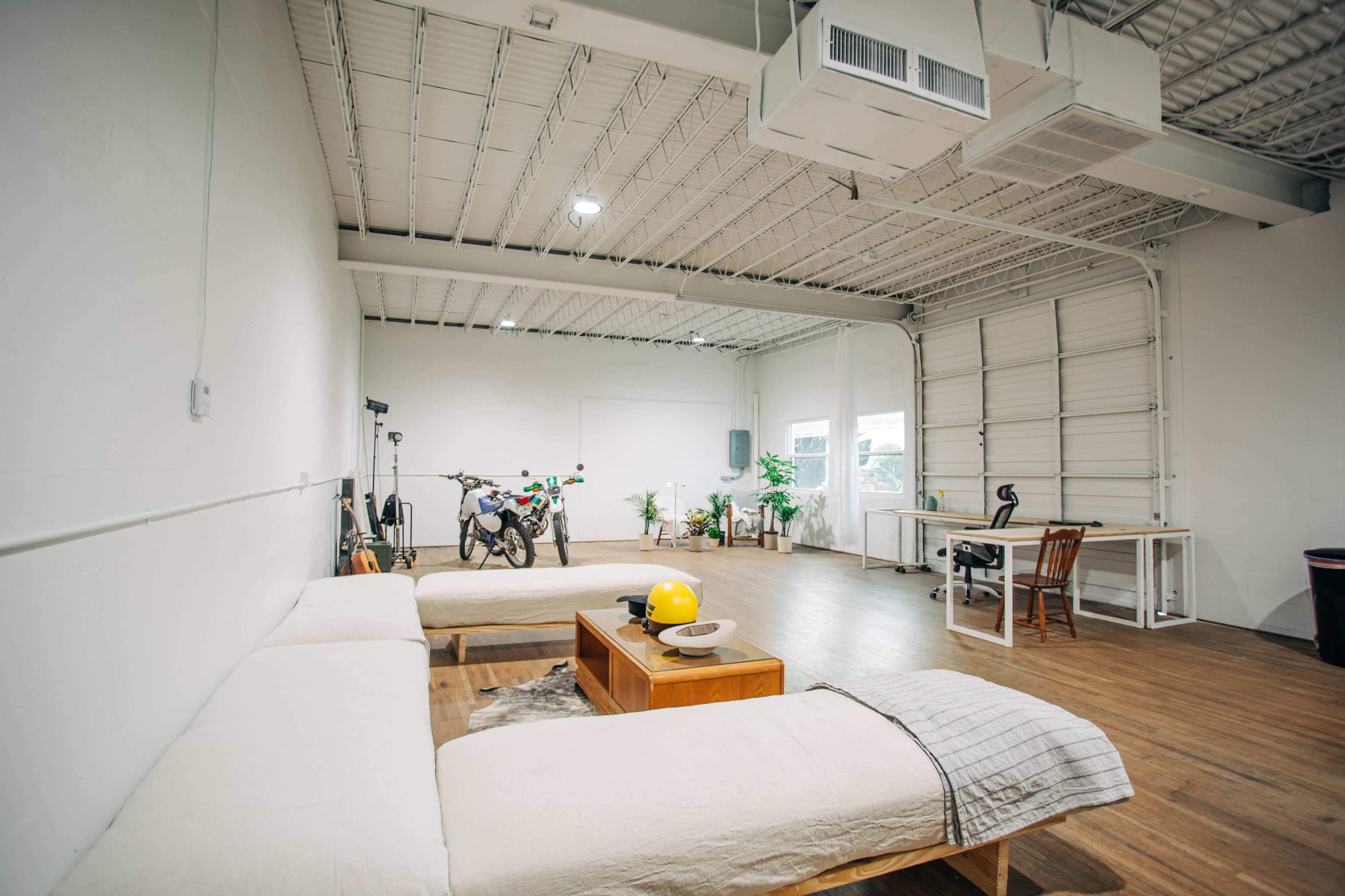 A spacious, minimalist room with a motorcycle parked in the background, a large sofa, a coffee table, and a desk with a chair.