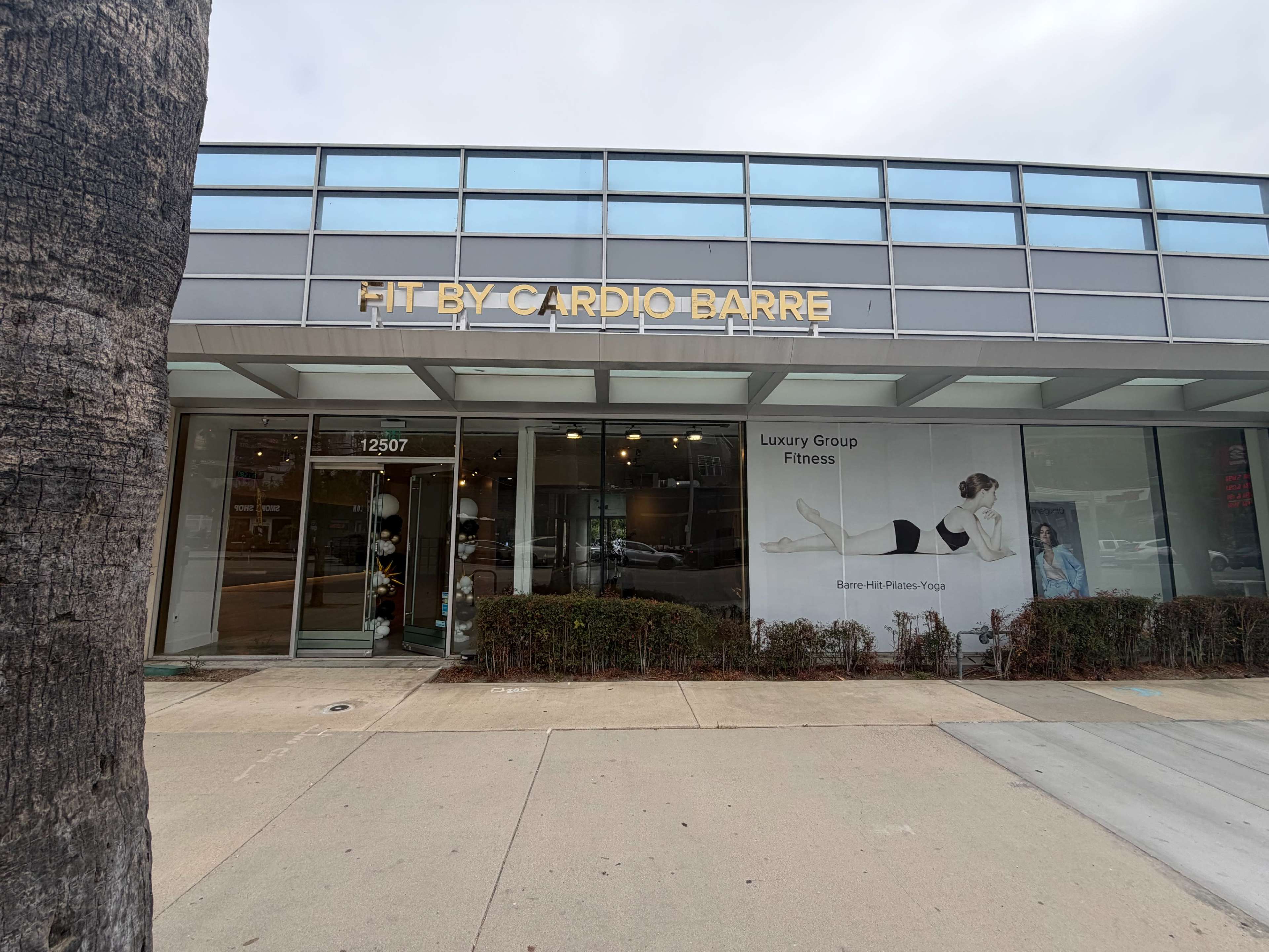 The image shows the exterior of a fitness studio called "Fit by Cardio Barre," featuring large windows and a modern design.