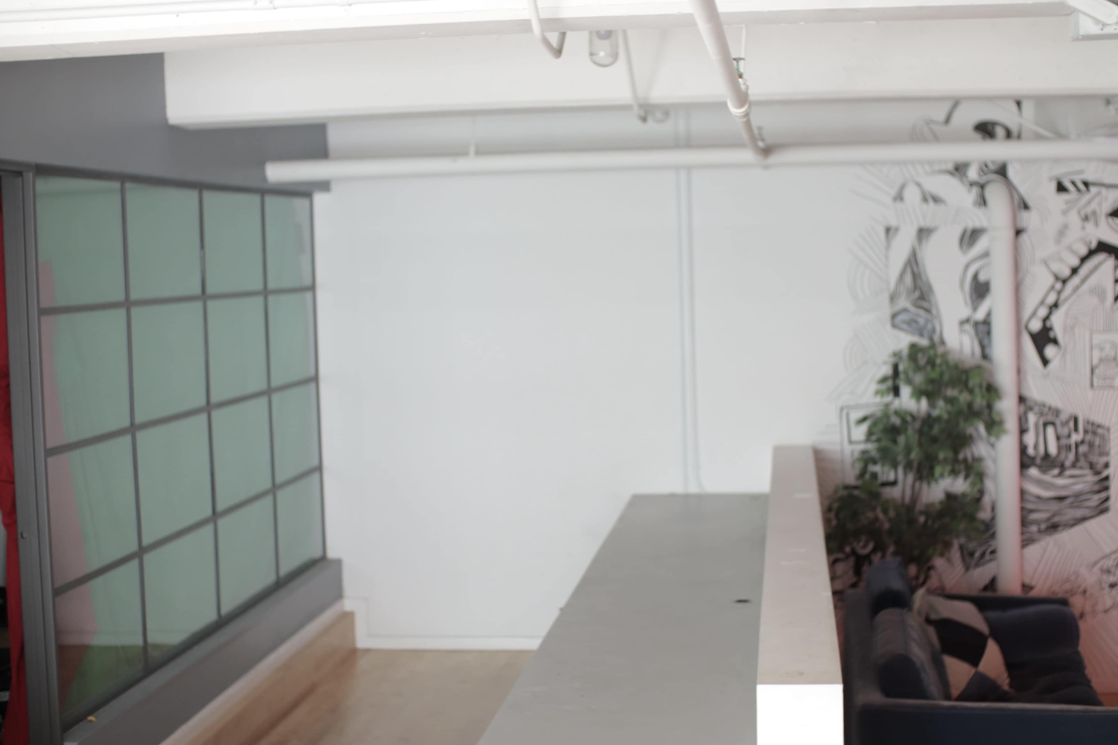 An airy interior space with a large, white counter, a glass wall on one side, and a mural on the opposite wall.