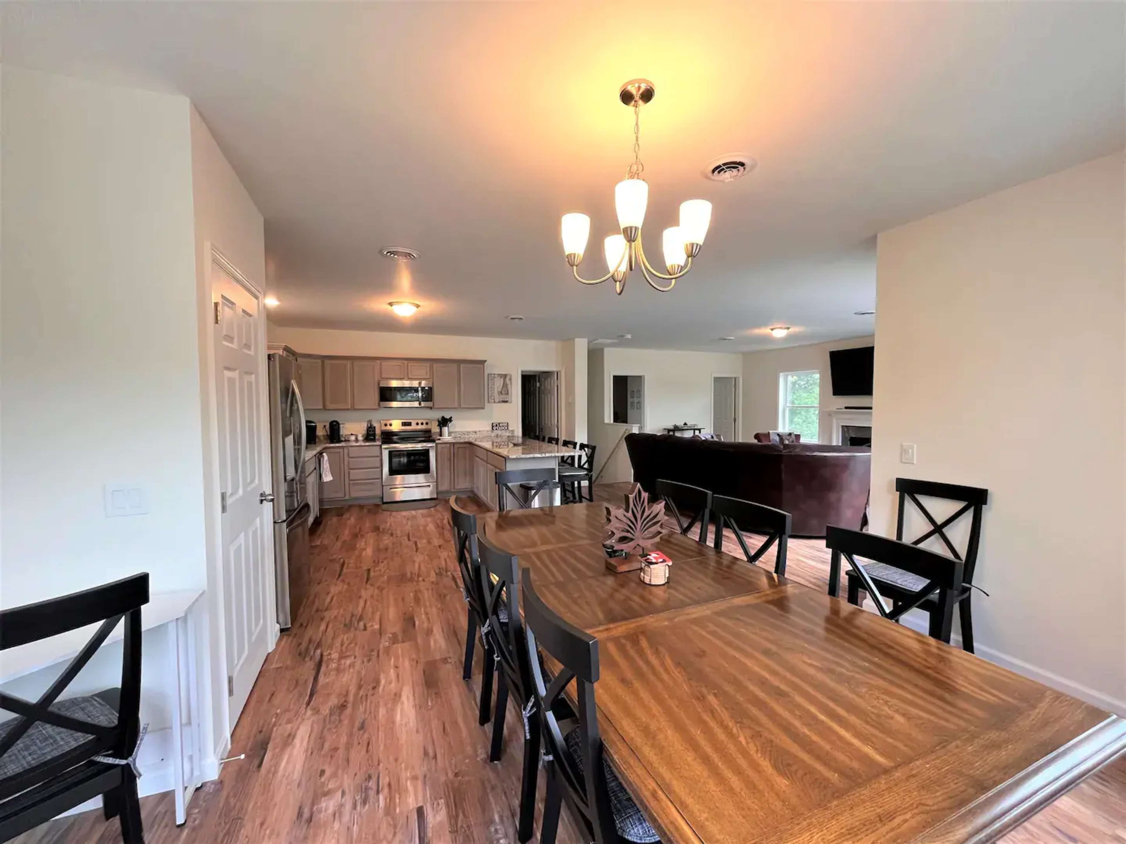 A spacious kitchen and dining area featuring a wooden dining table, stainless steel appliances, and a chandelier overhead.