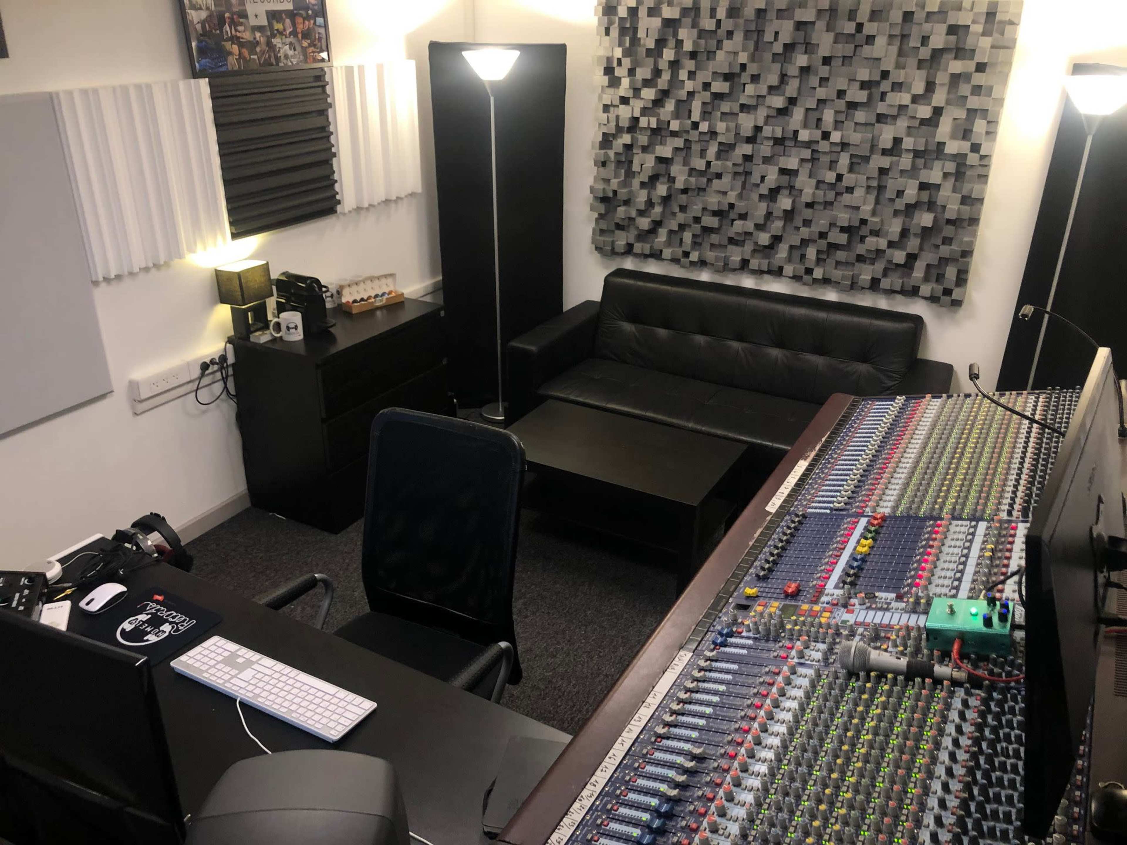A control room setup with audio mixing equipment, a black sofa, and soundproofing panels on the walls.