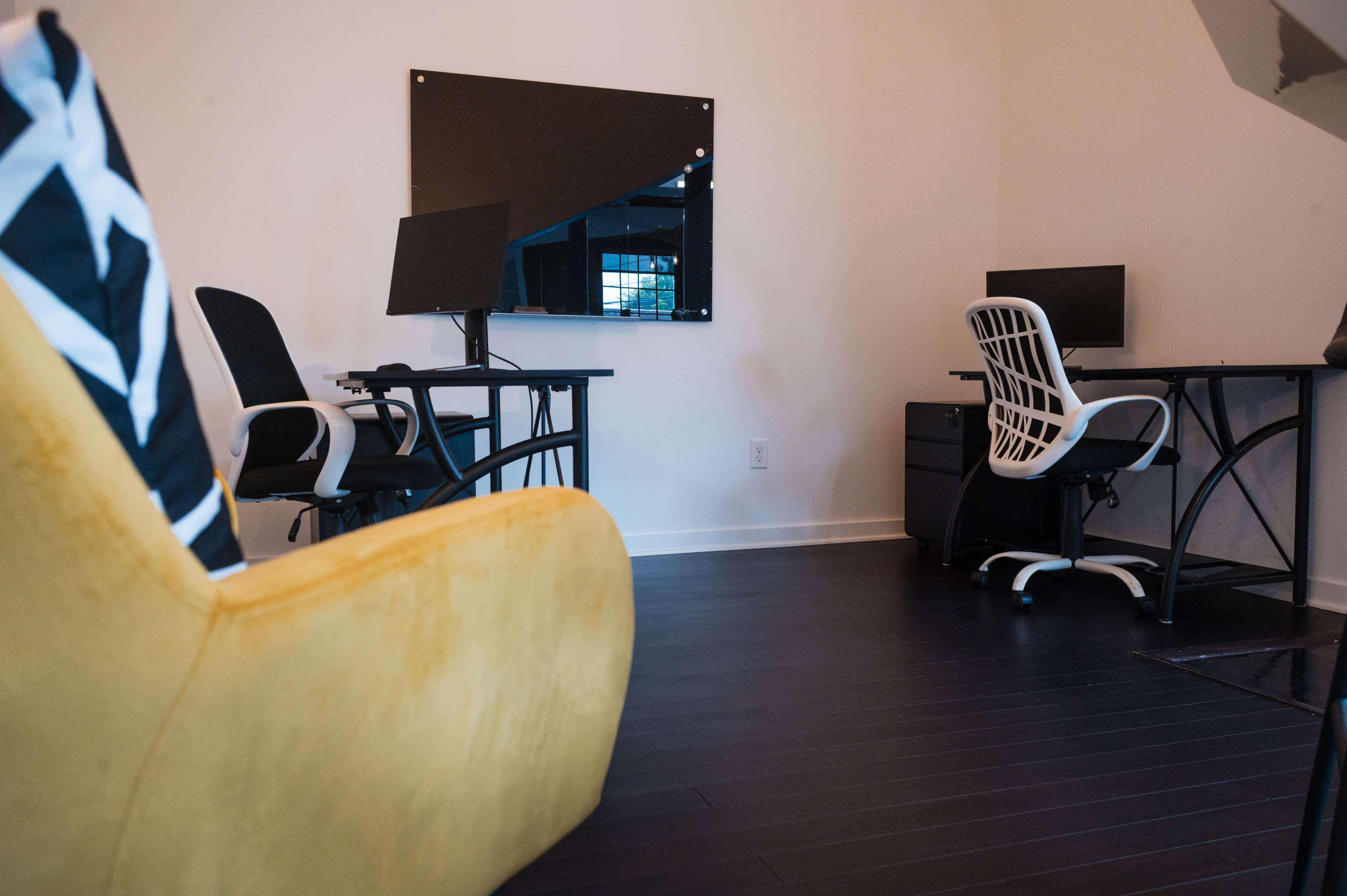 A modern office space featuring two desks with computers, a large mirror, and a yellow chair in the foreground.