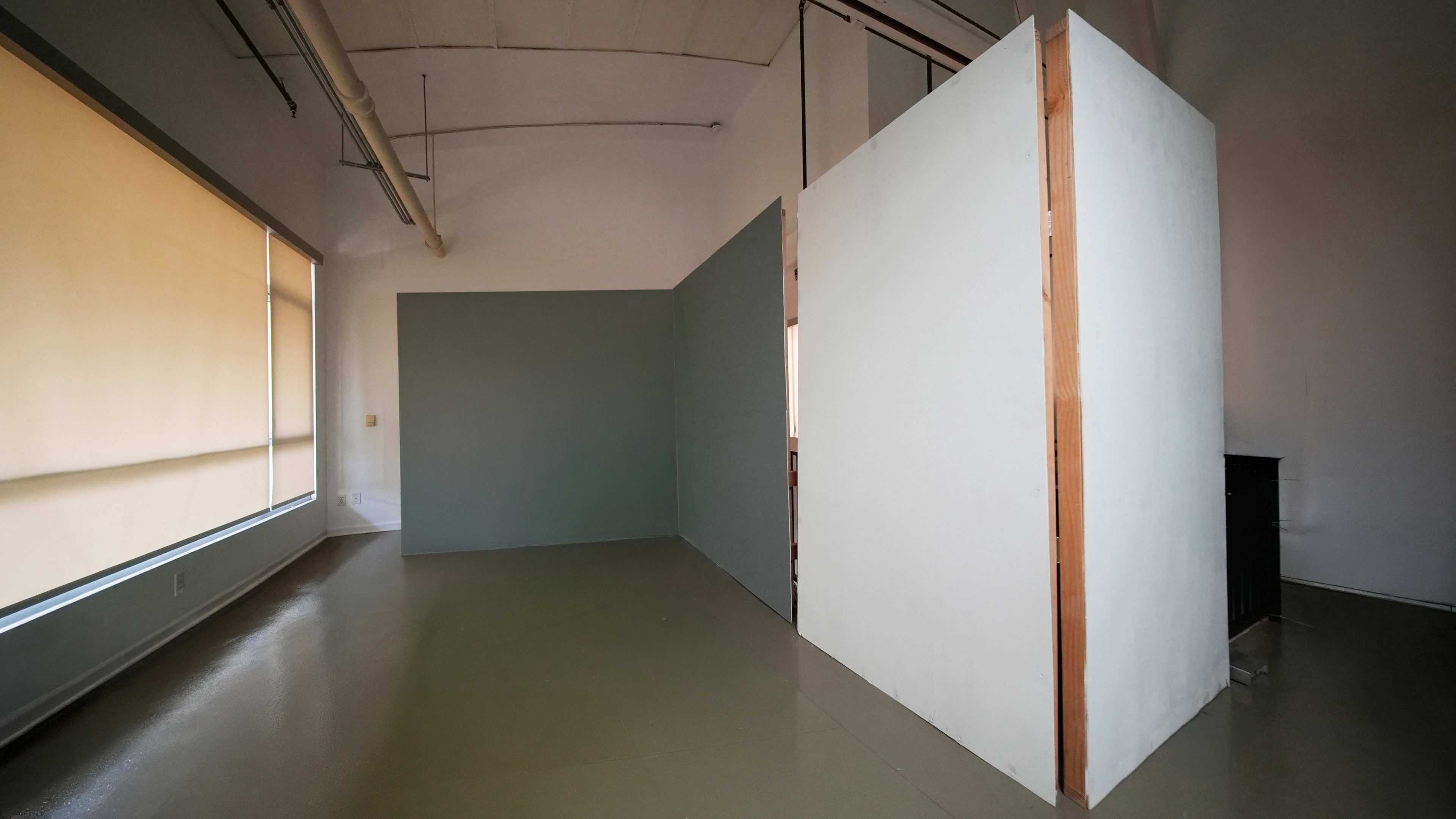 The image shows a spacious indoor area with plain walls and a distinct division created by a partition in the center.