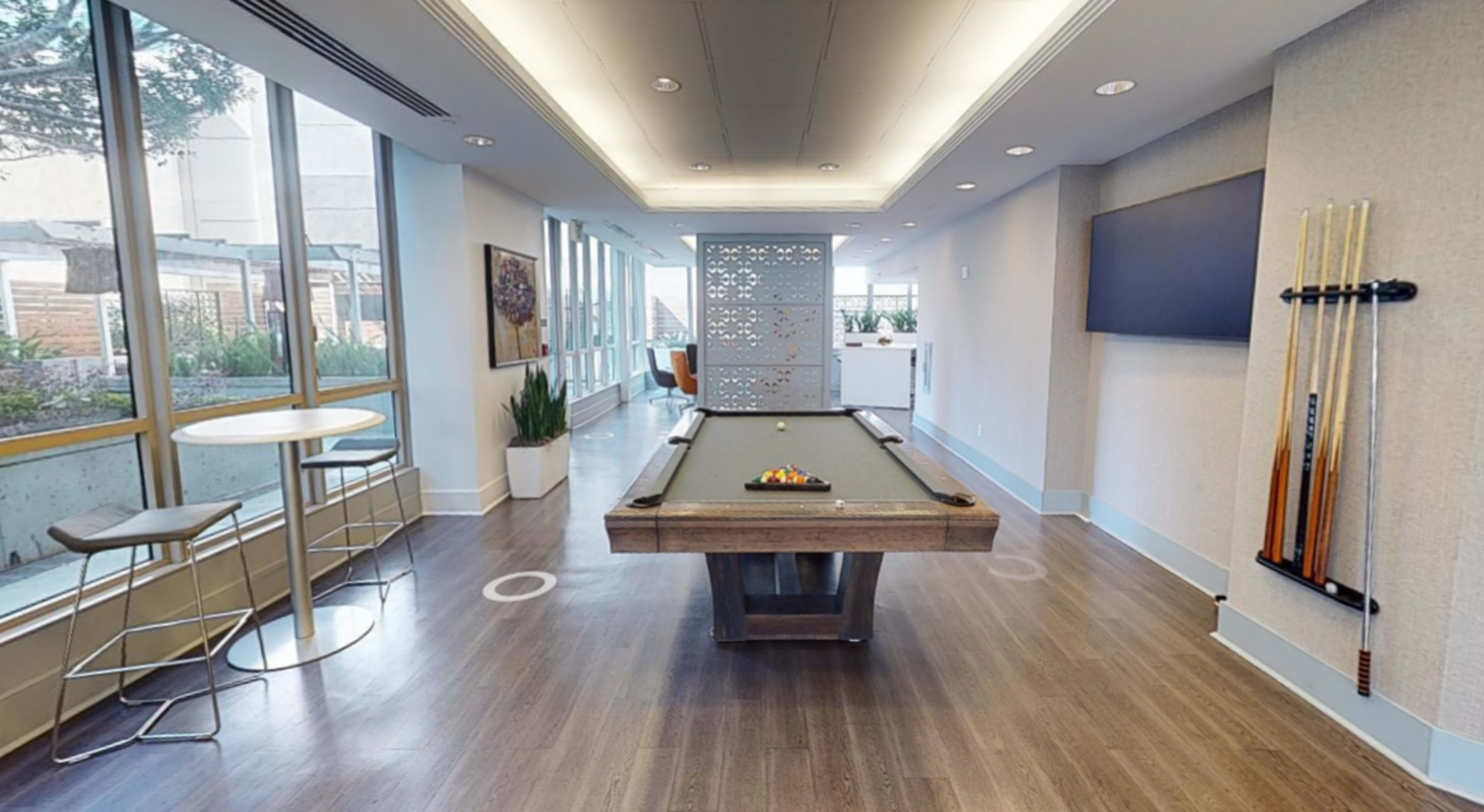 A spacious game room featuring a pool table in the center, surrounded by large windows and contemporary furnishings.