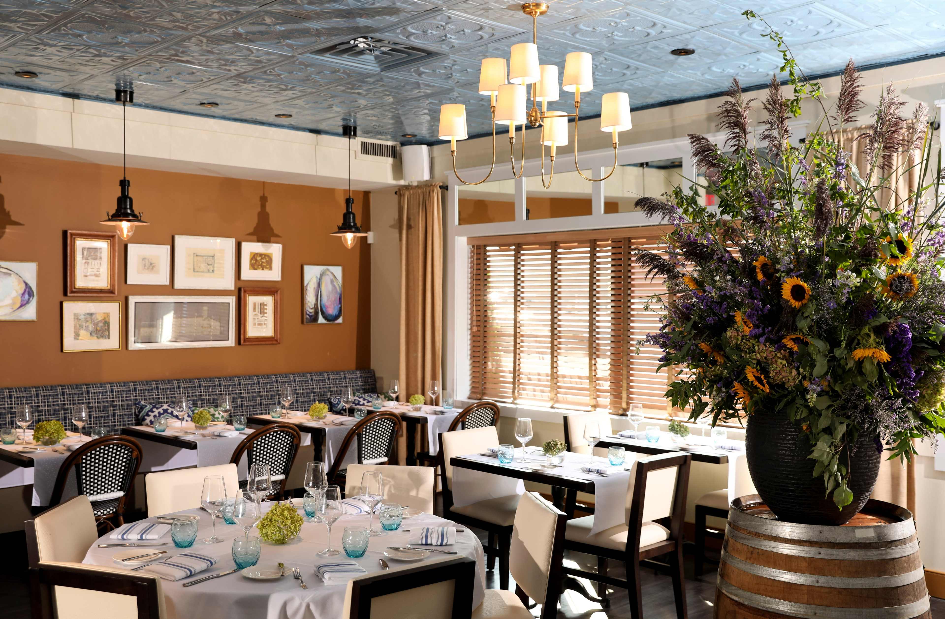 A dining area in a restaurant with elegantly set tables, a large floral arrangement, and a combination of modern and rustic decor elements.