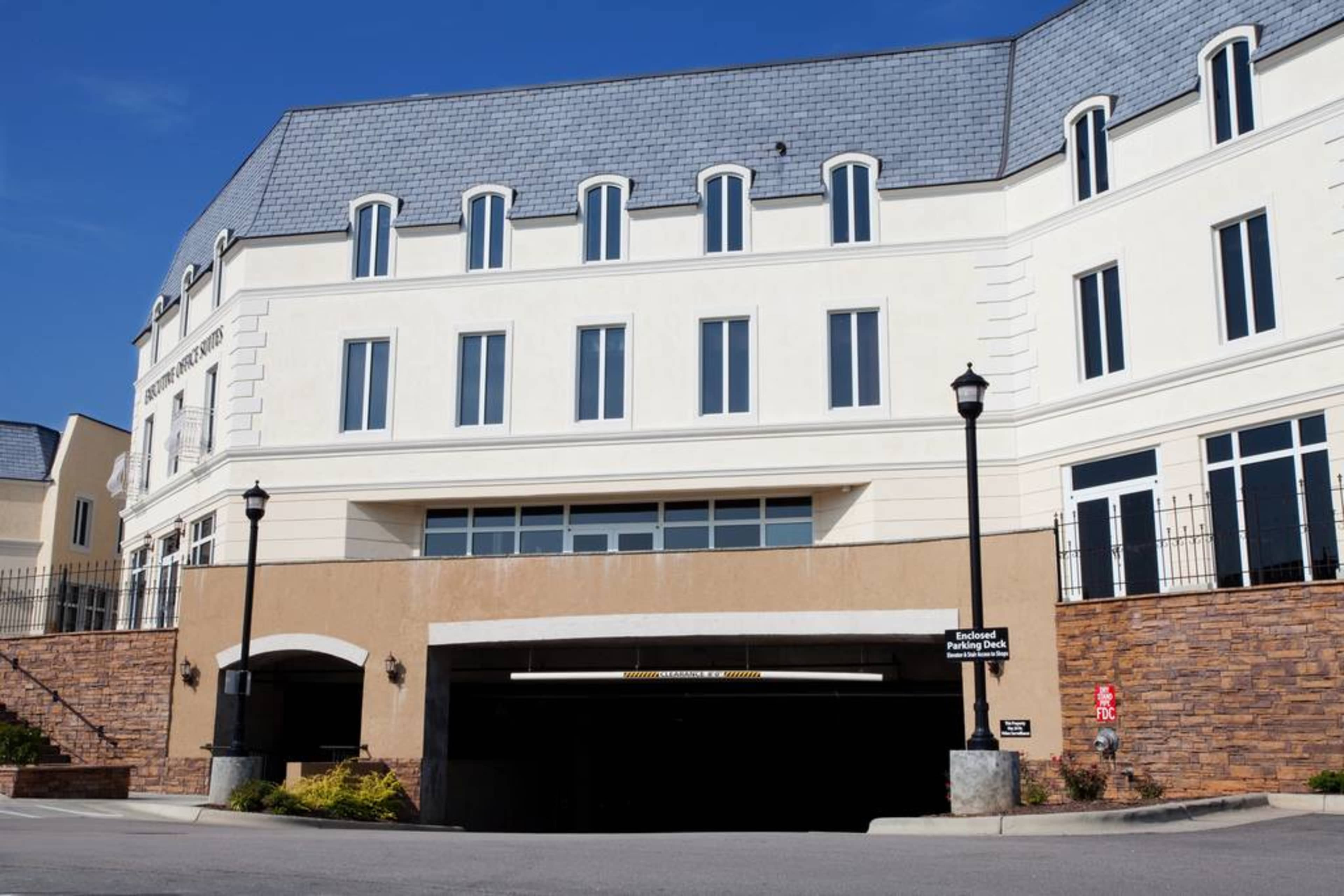 A multi-story building with a parking garage entrance at its base, featuring a light-colored exterior and several windows.