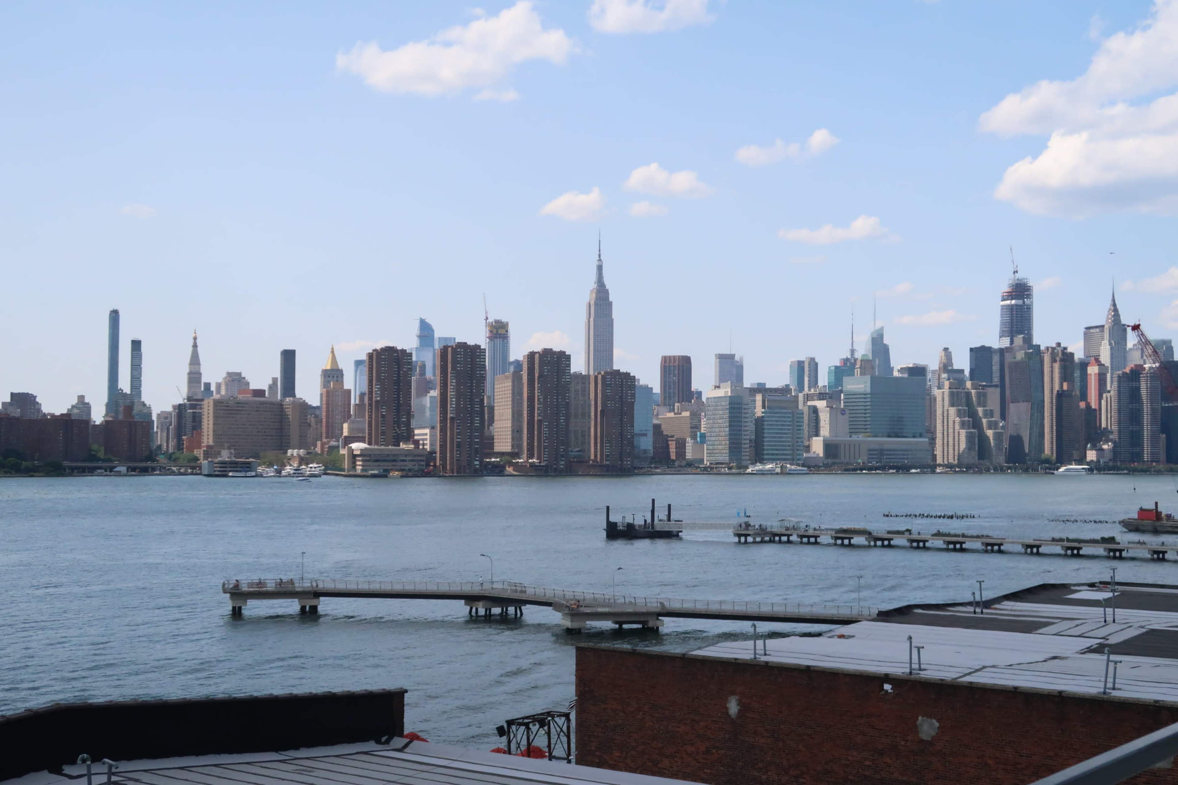A view of the Manhattan skyline across a body of water, with various buildings and the Empire State Building prominently visible.