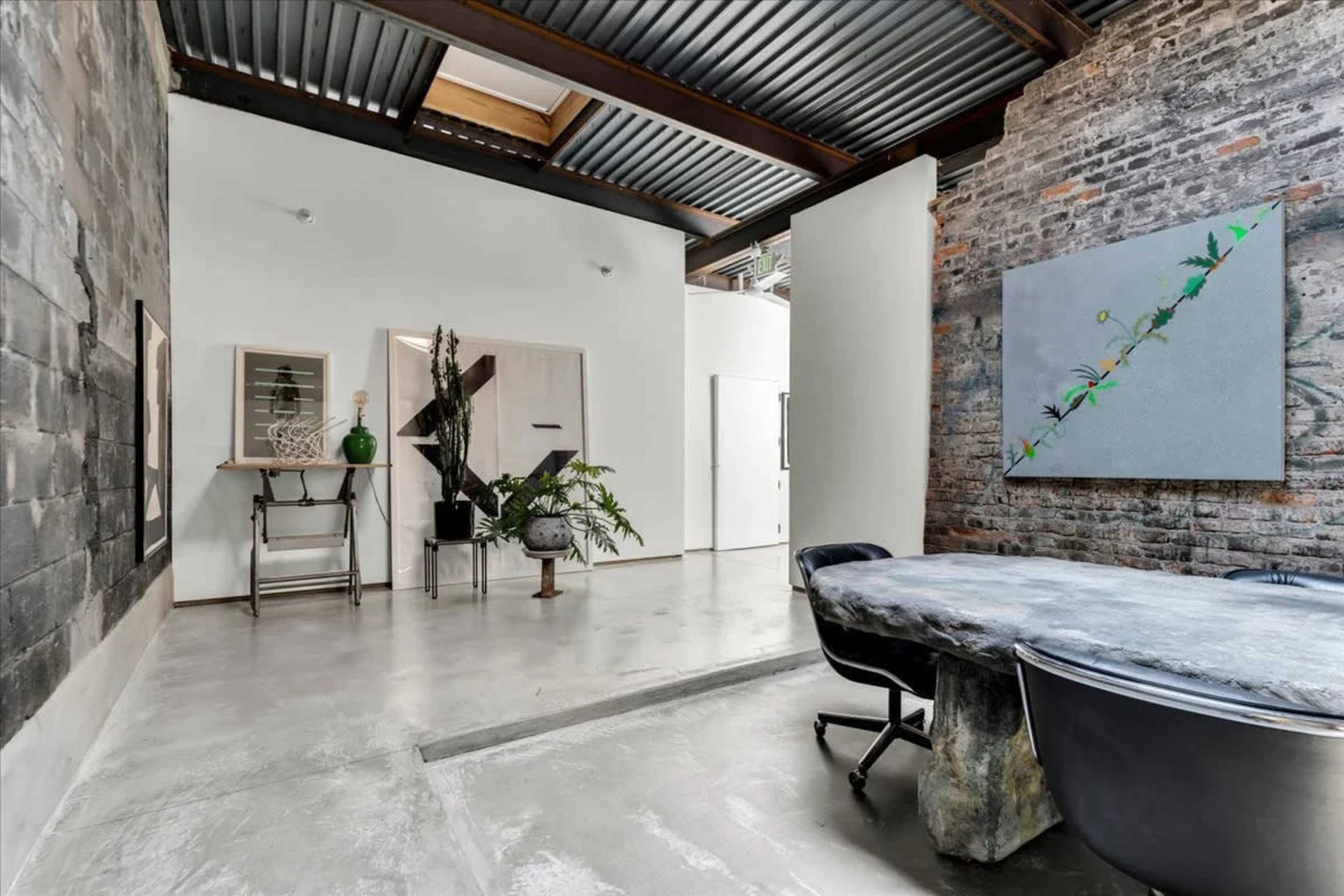 The image shows a modern, industrial-style interior space featuring exposed brick walls, a concrete floor, and a large table surrounded by black chairs.