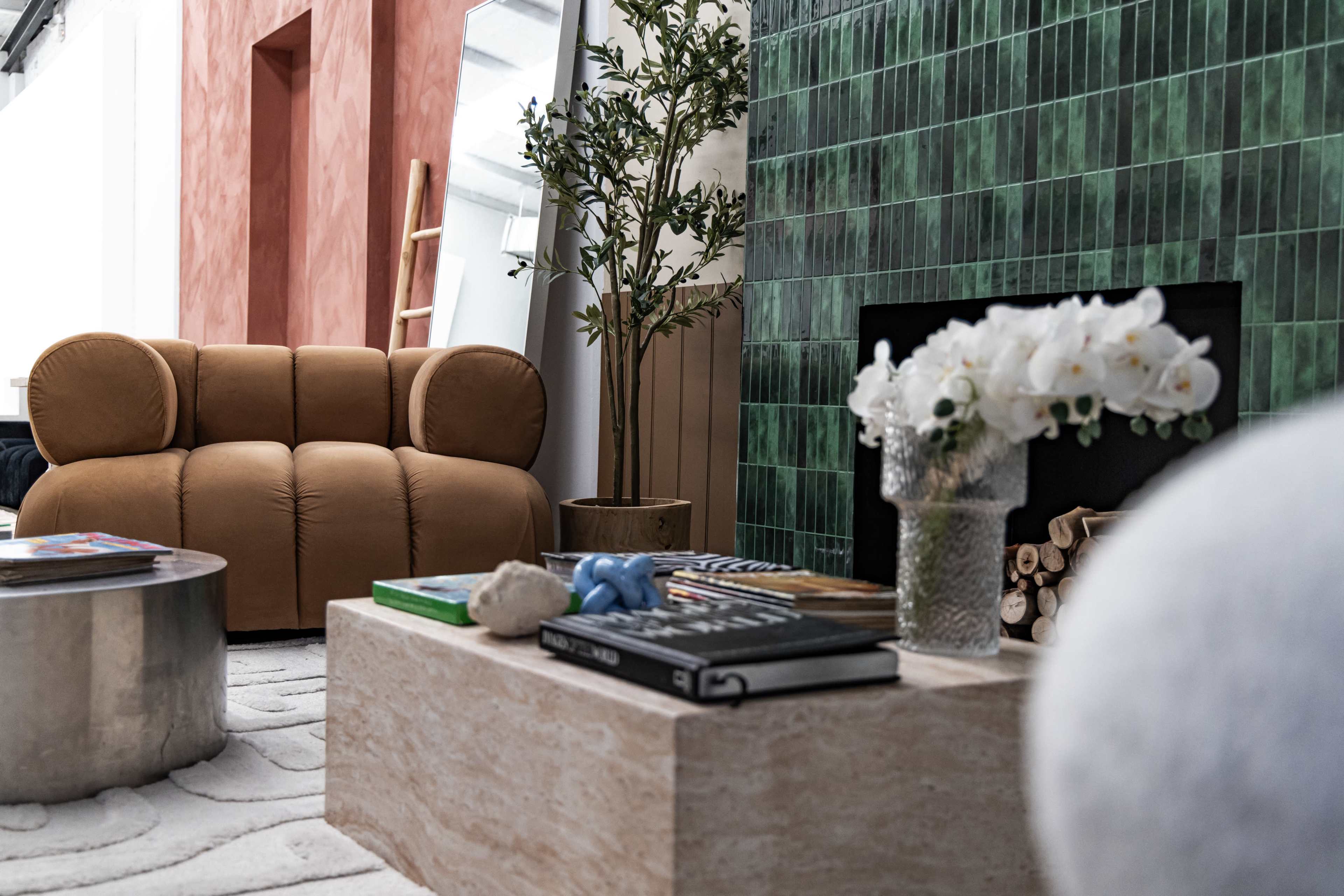 The scene features a cozy living room with a brown, rounded sofa, a marble coffee table with books and decor, and a vibrant green tiled wall.