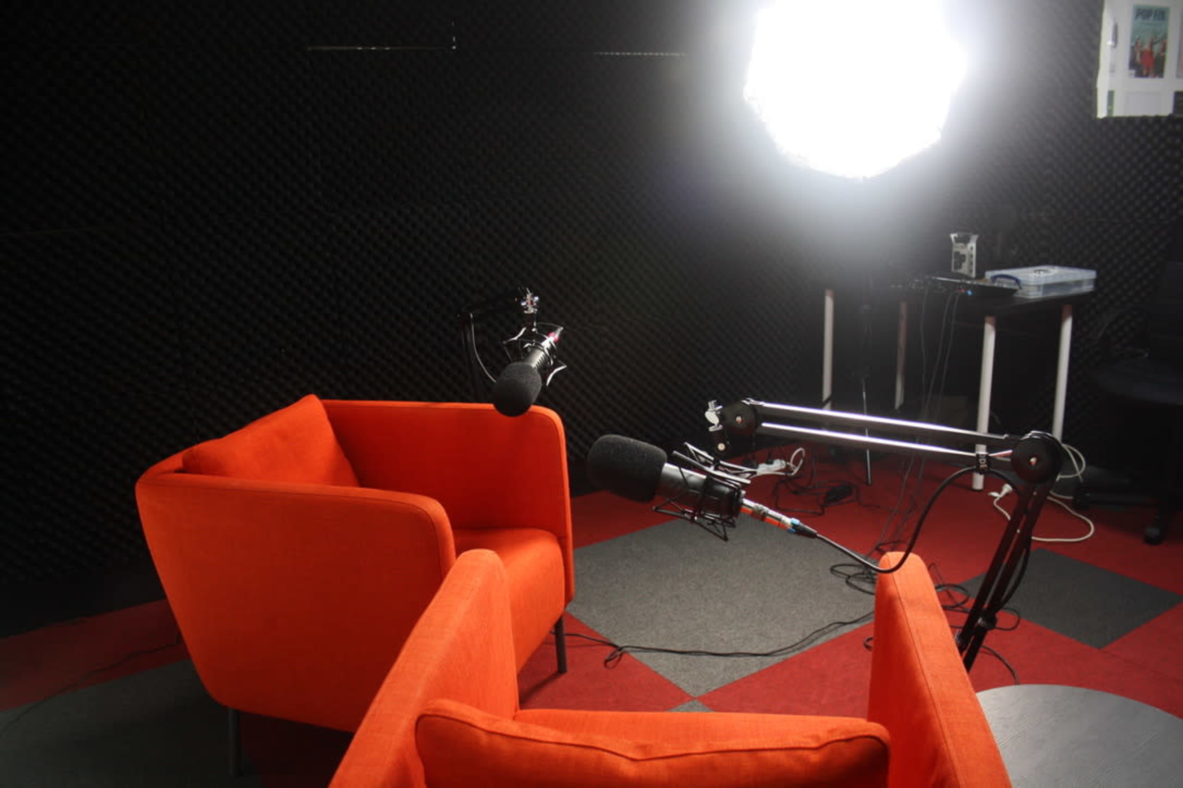 Two orange chairs facing each other under bright lighting in a soundproof studio with black acoustic panels.