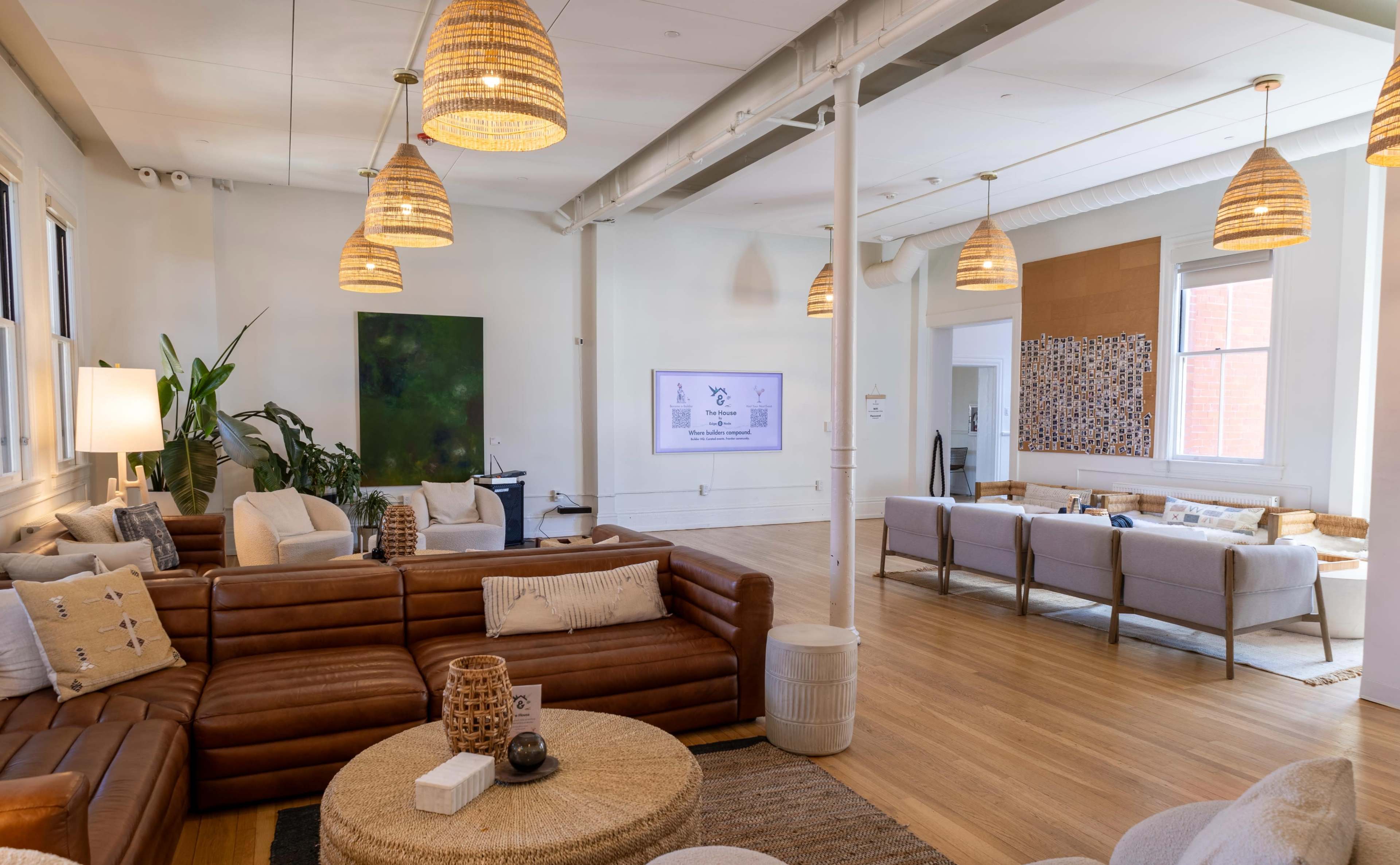 The image shows a spacious, modern lounge area with a leather sofa, decorative lighting, and a large screen on the wall.