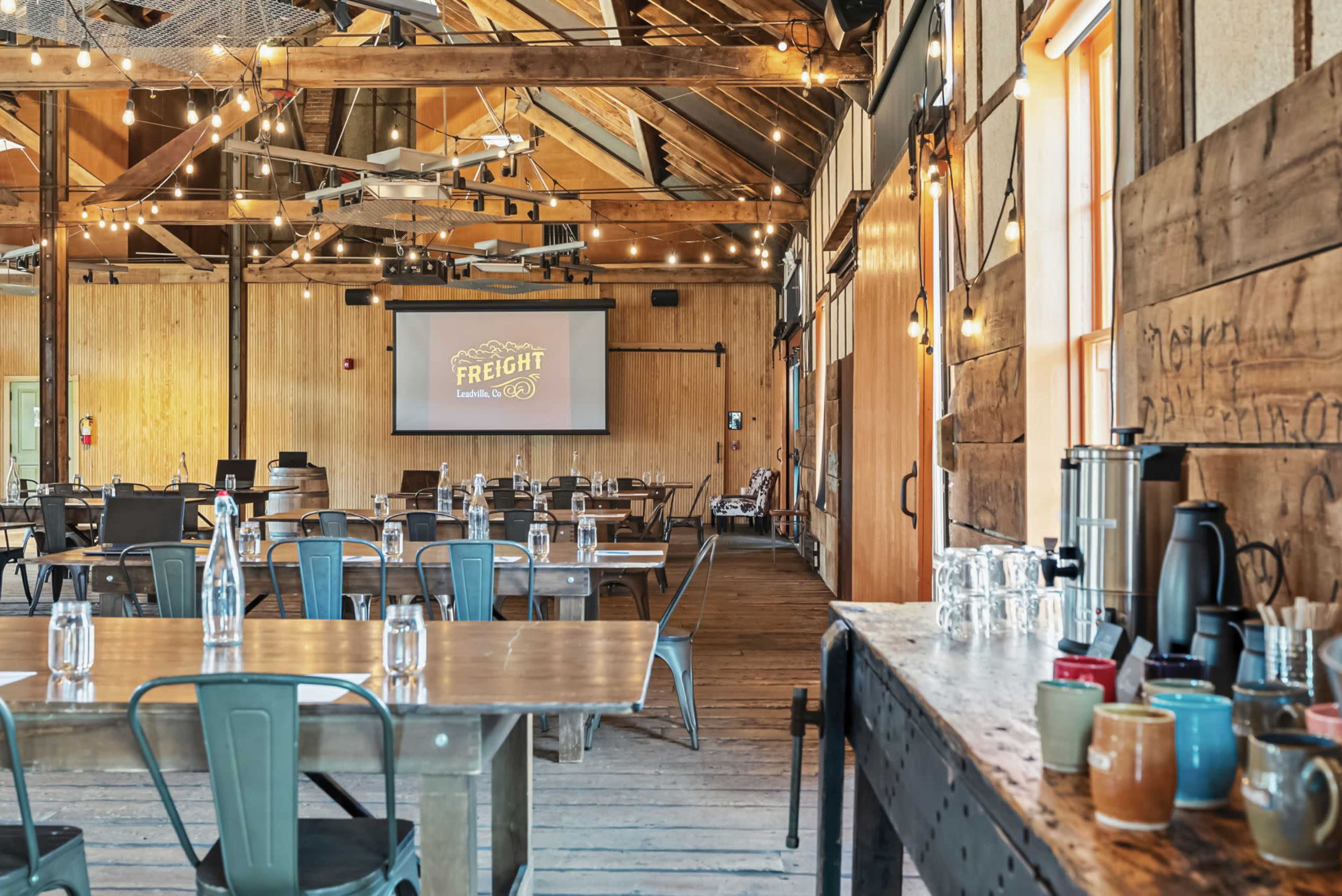 The image shows a rustic event space with wooden beams, multiple tables set with glassware, and a projector screen displaying "FREIGHT" on one wall.