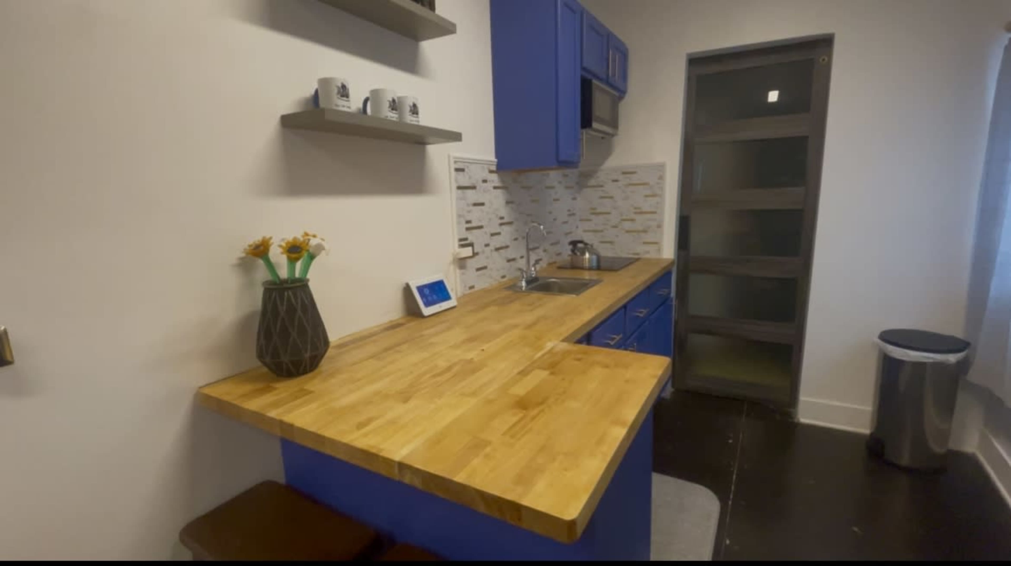 The image shows a compact kitchen featuring blue cabinetry, a wooden countertop, and modern appliances.
