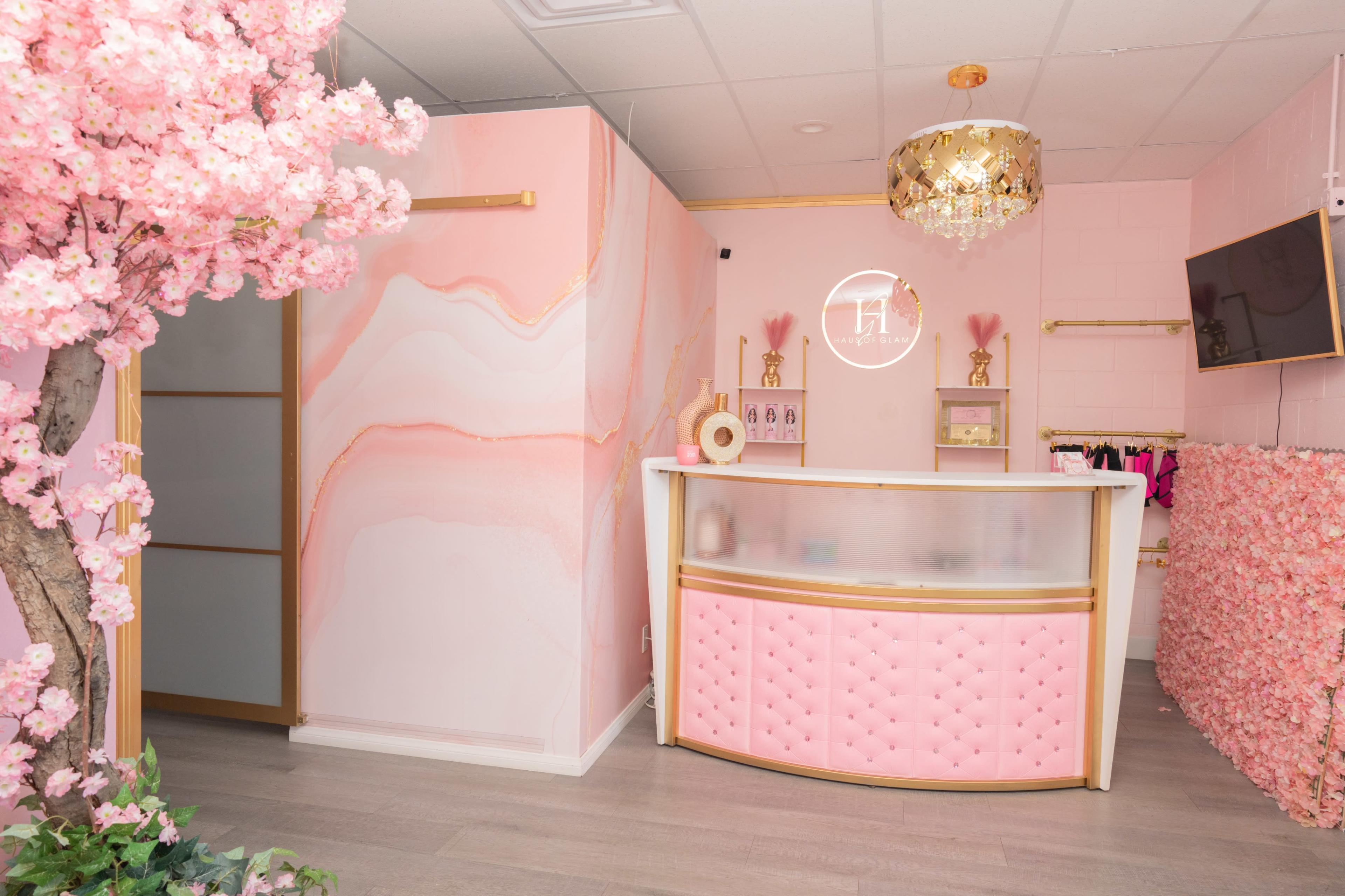 A retail space with a pink and gold color scheme, featuring a reception desk, floral decorations, and a chandelier.