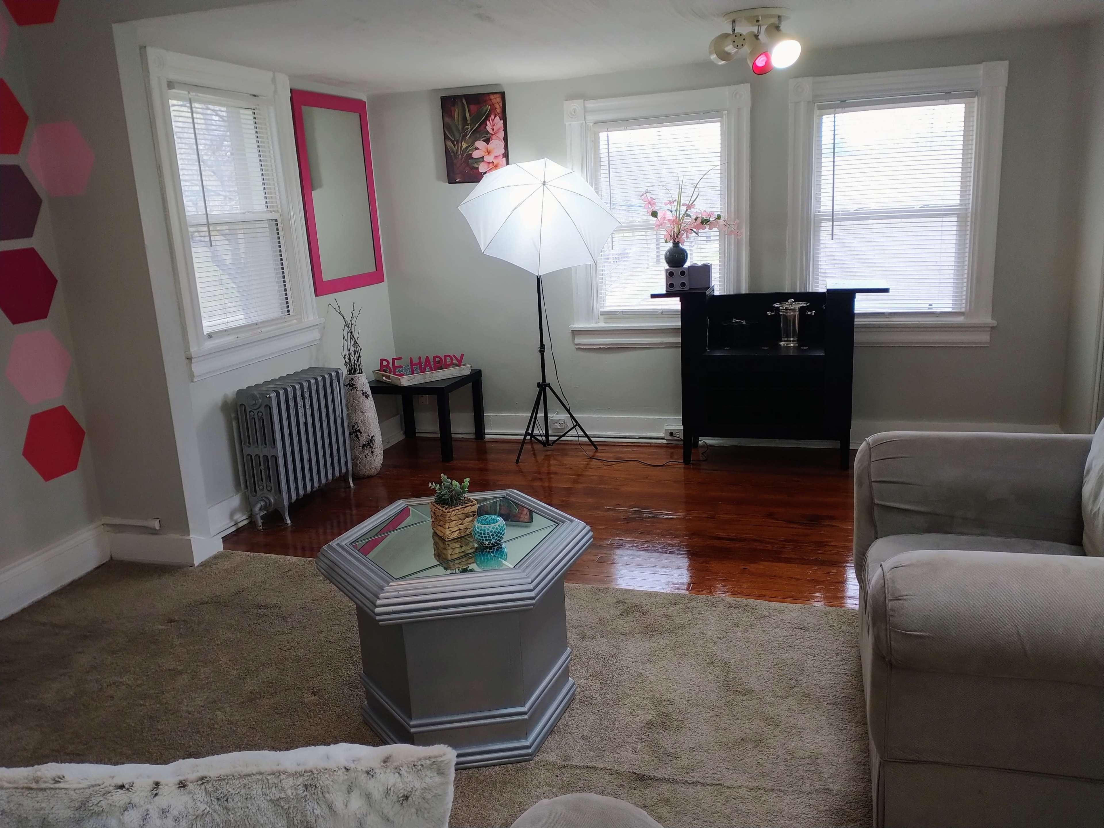 A living room featuring a beige sofa, a coffee table, a floor lamp, and a small black console table beside large windows.