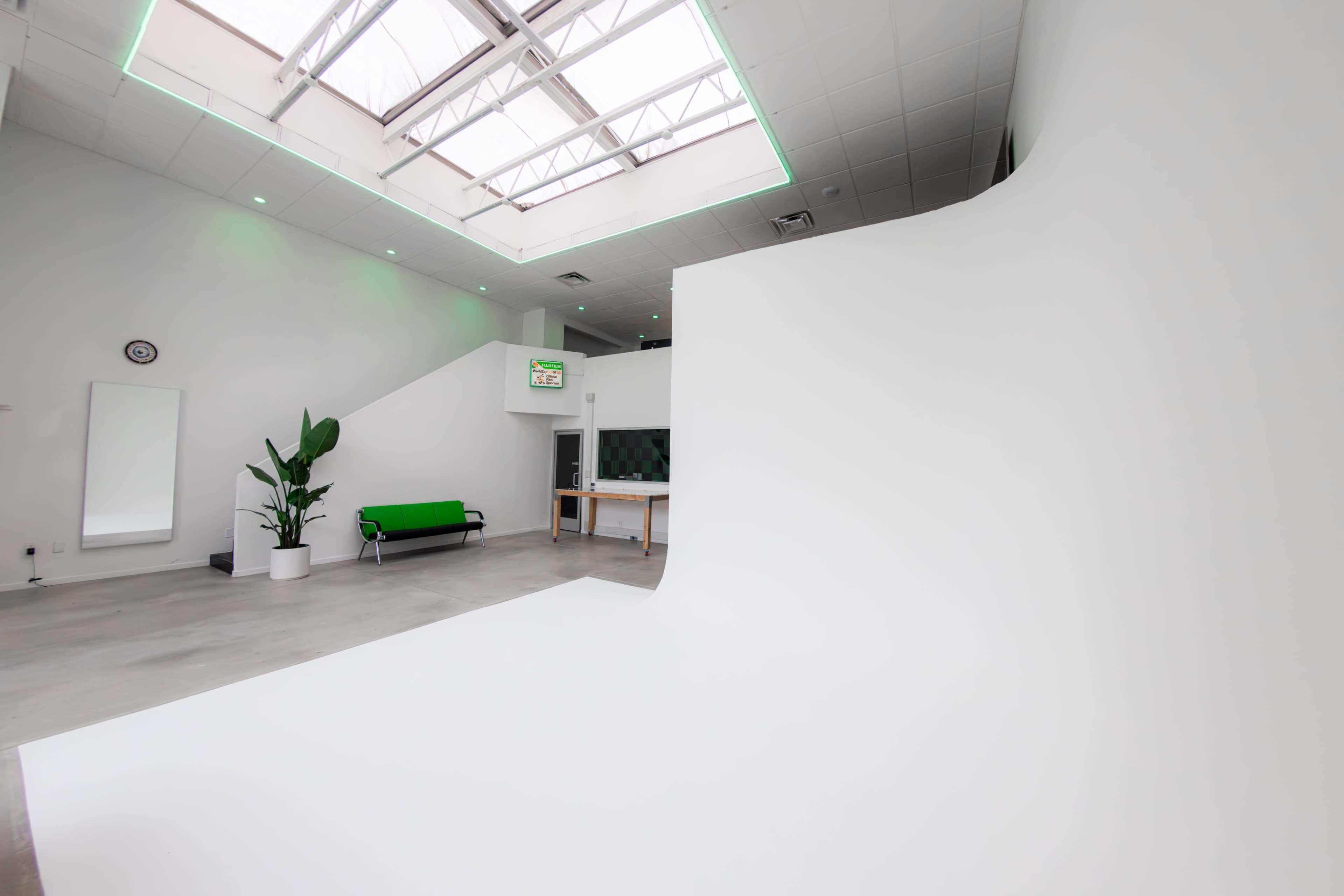 An interior space featuring a minimalist design with a green sofa, a potted plant, a staircase, and large skylights.
