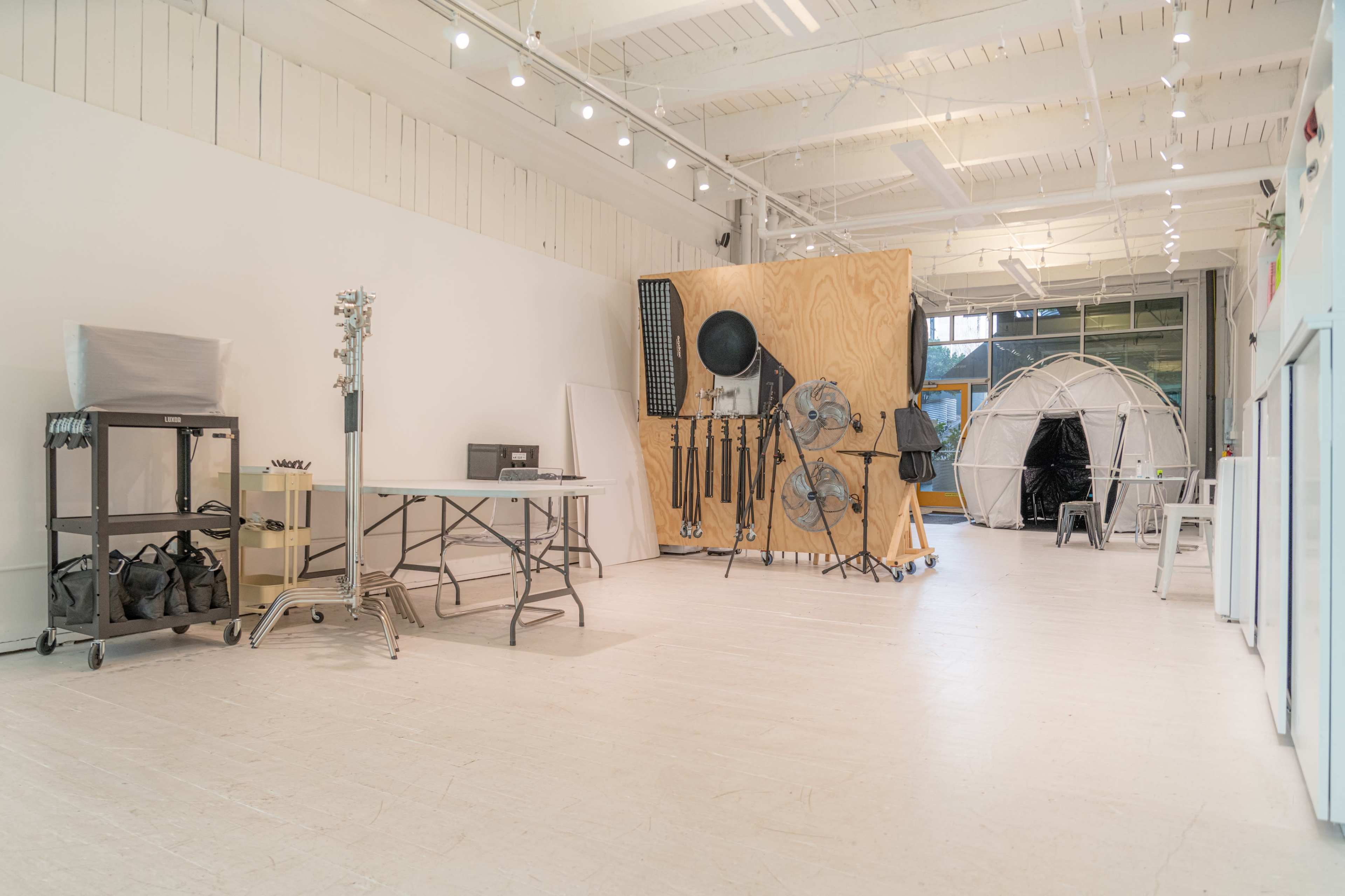 A spacious studio with white walls and a wooden partition, containing various equipment and a tent-like structure in one corner.
