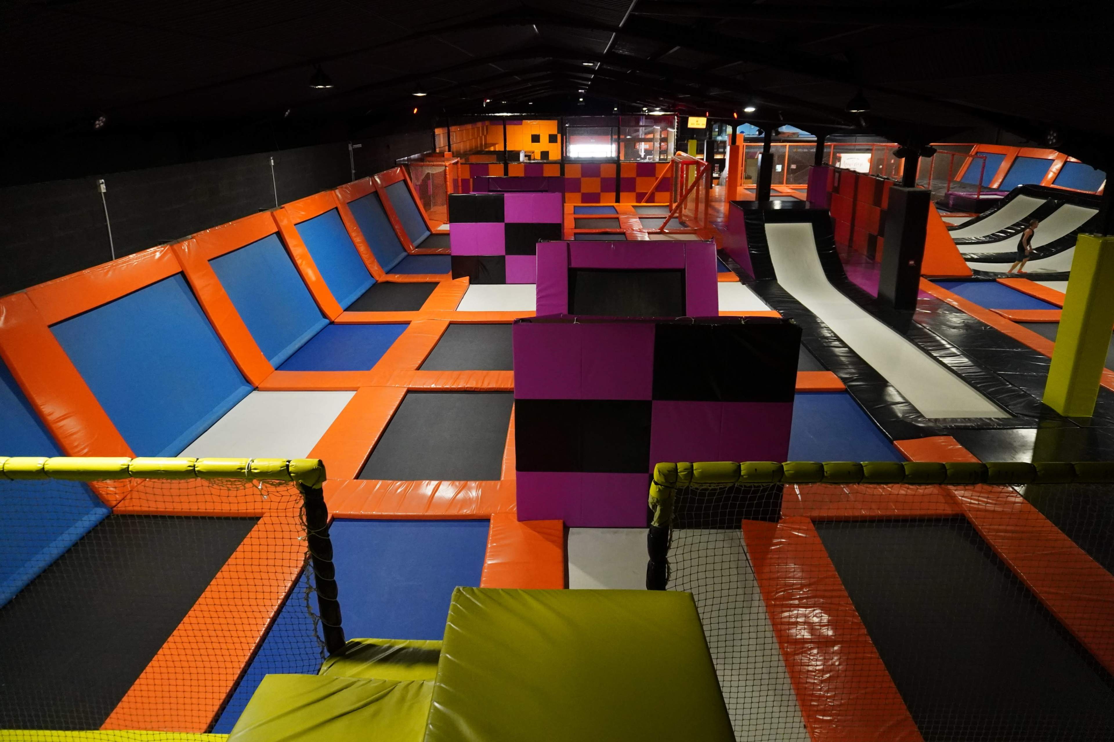 An indoor trampoline park featuring multiple trampolines, foam pits, and colorful safety pads arranged throughout the space.