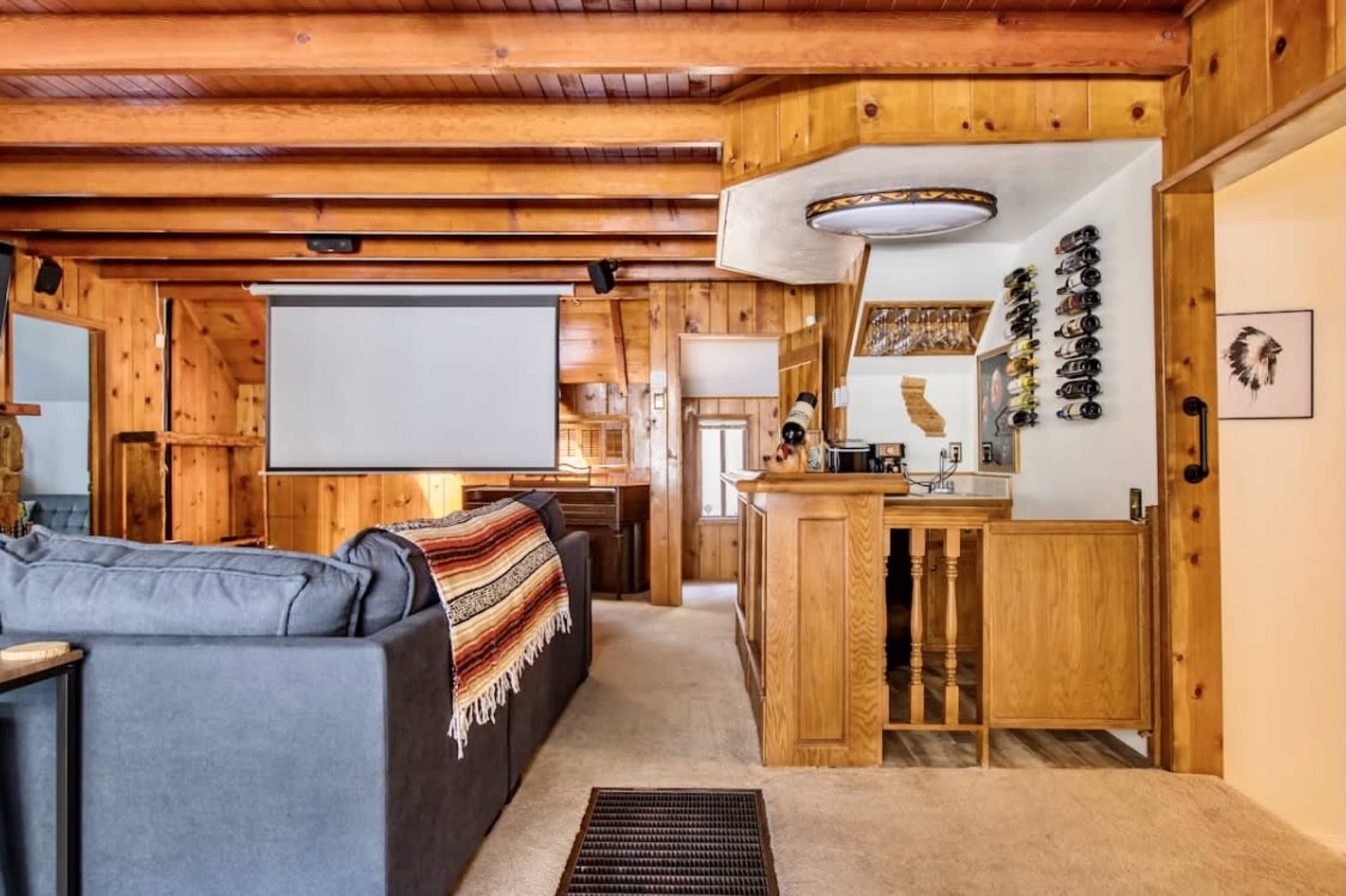 The room features wooden paneling, a sectional couch, a beverage bar, and a projector screen mounted on the wall.