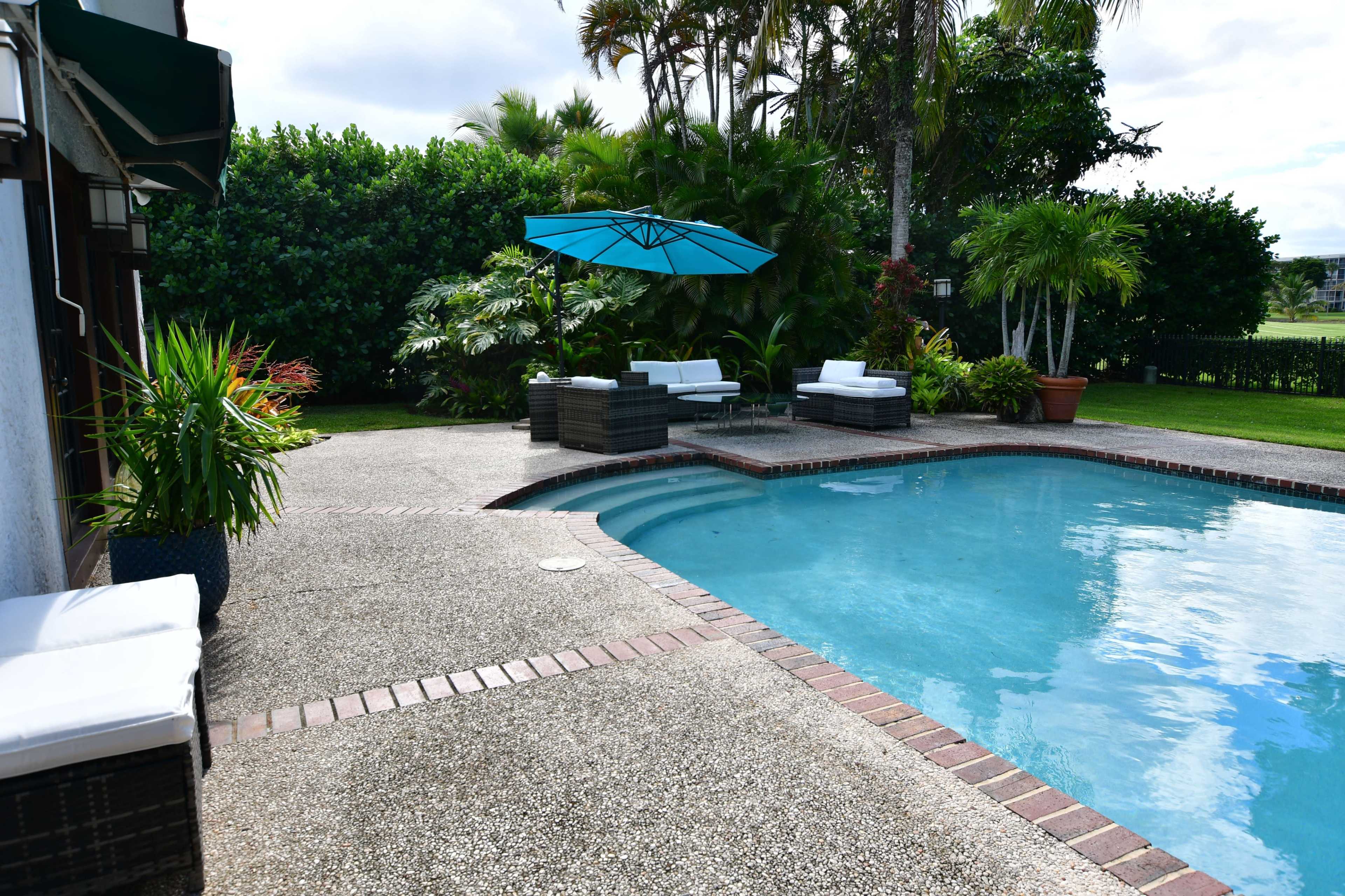 A swimming pool with a curved edge surrounded by patio furniture and tropical plants.