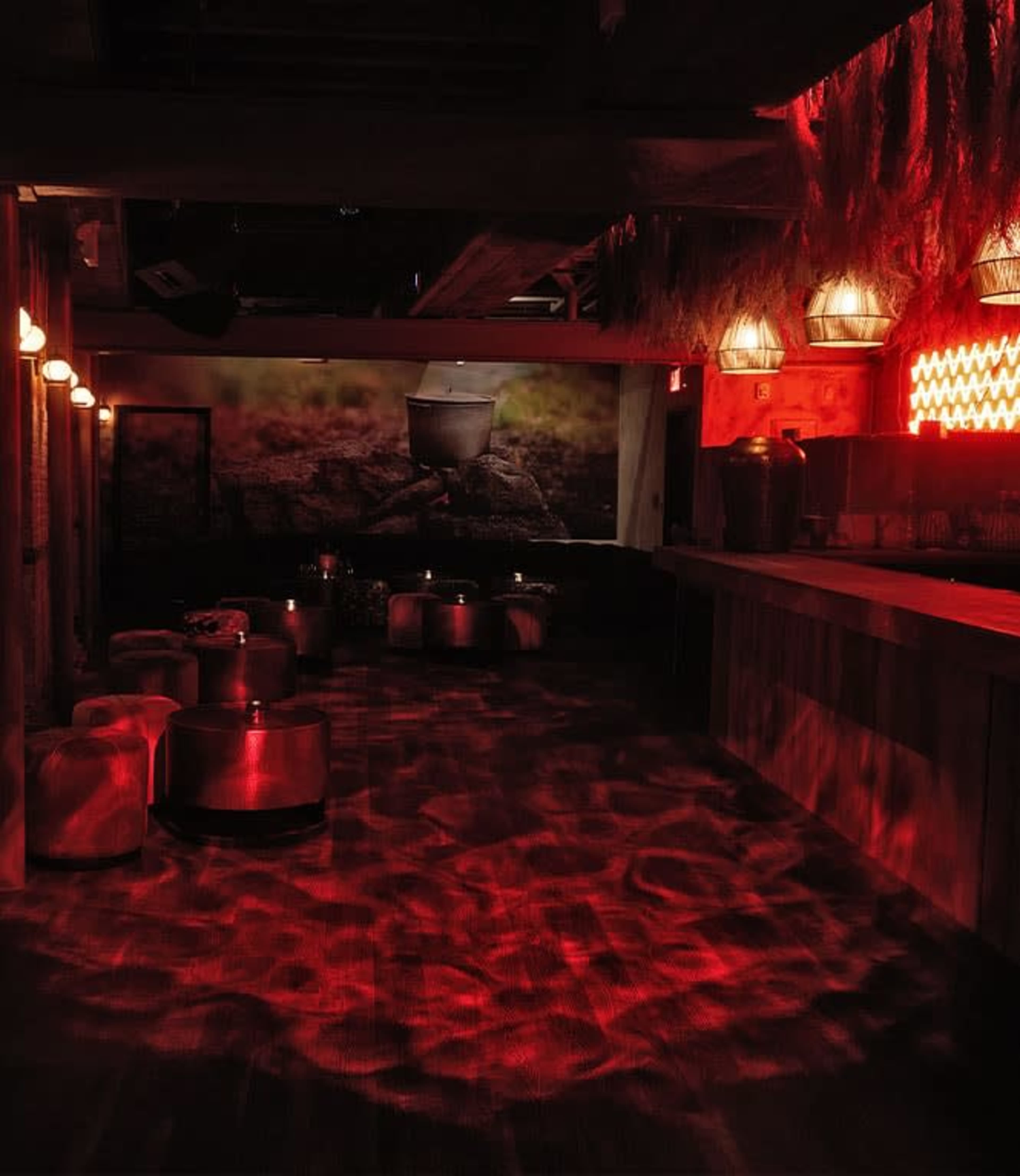 The image shows a dimly lit room with red lighting, featuring a bar area and several seating arrangements on the floor.