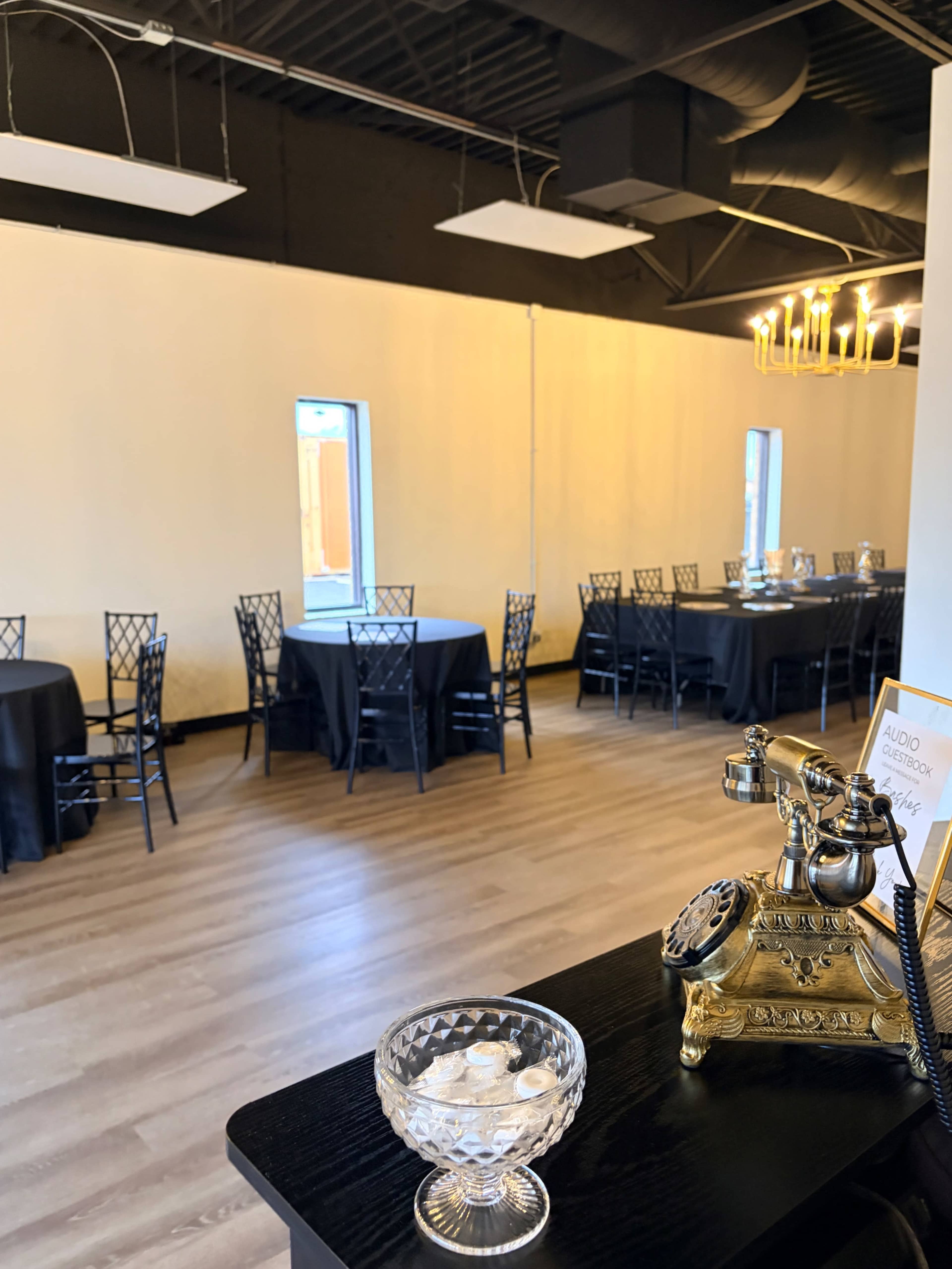 The image shows a dining area with several black-covered tables and chairs, illuminated by overhead lights.