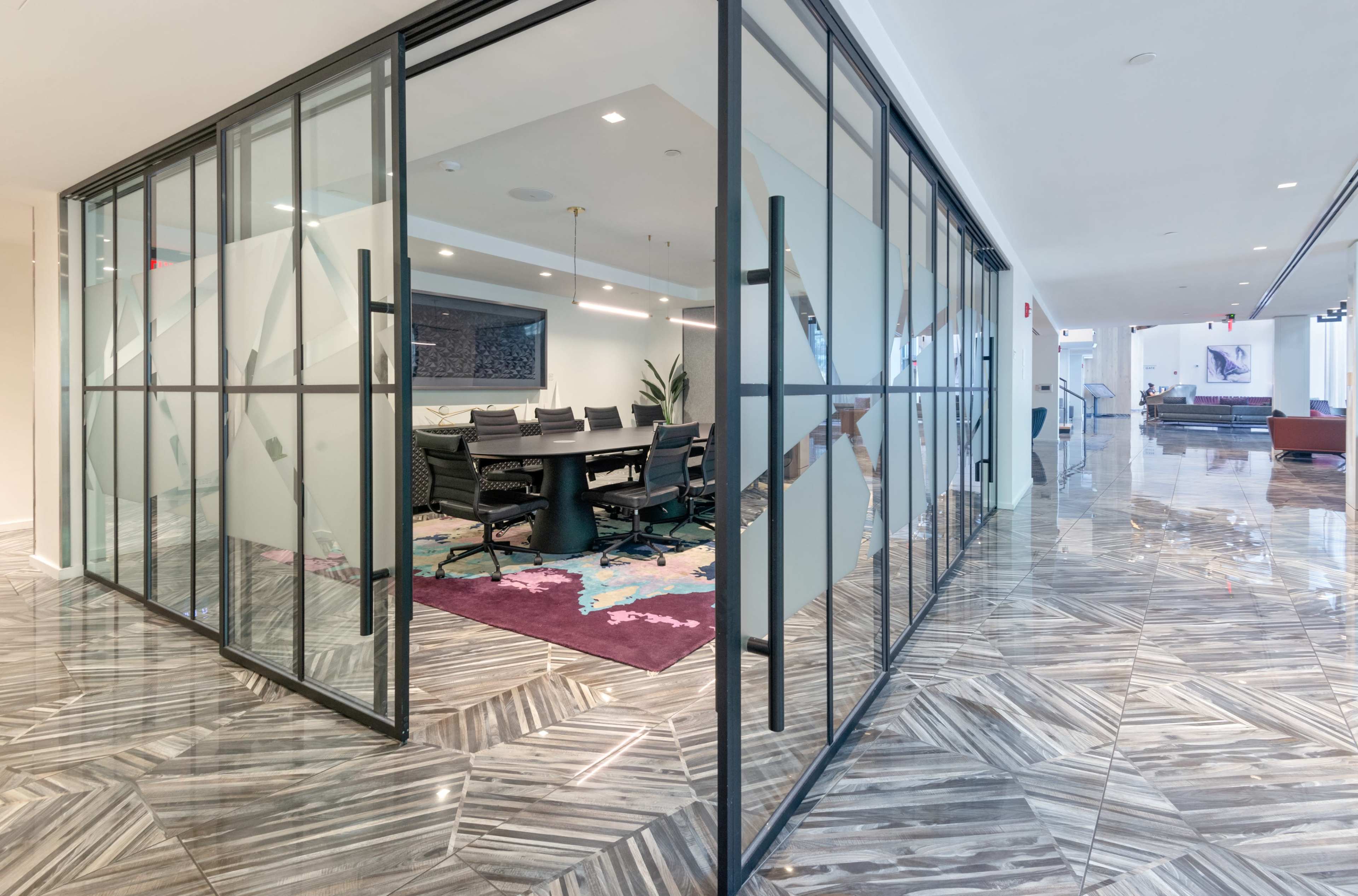 The image shows a modern office space featuring a glass-walled conference room with a long table and chairs, alongside a shiny tiled floor.