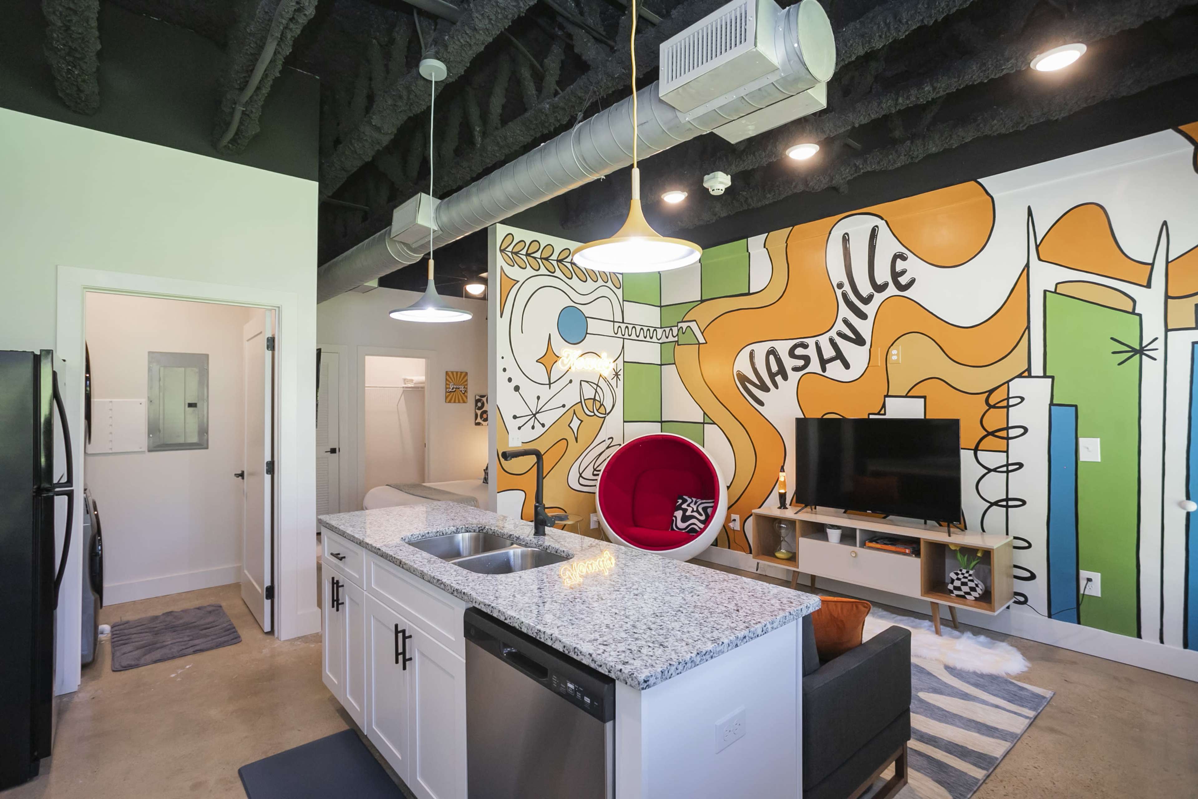 A modern kitchen and living area feature a vibrant mural reading "Nashville" on one wall, with a red accent chair and contemporary furnishings.
