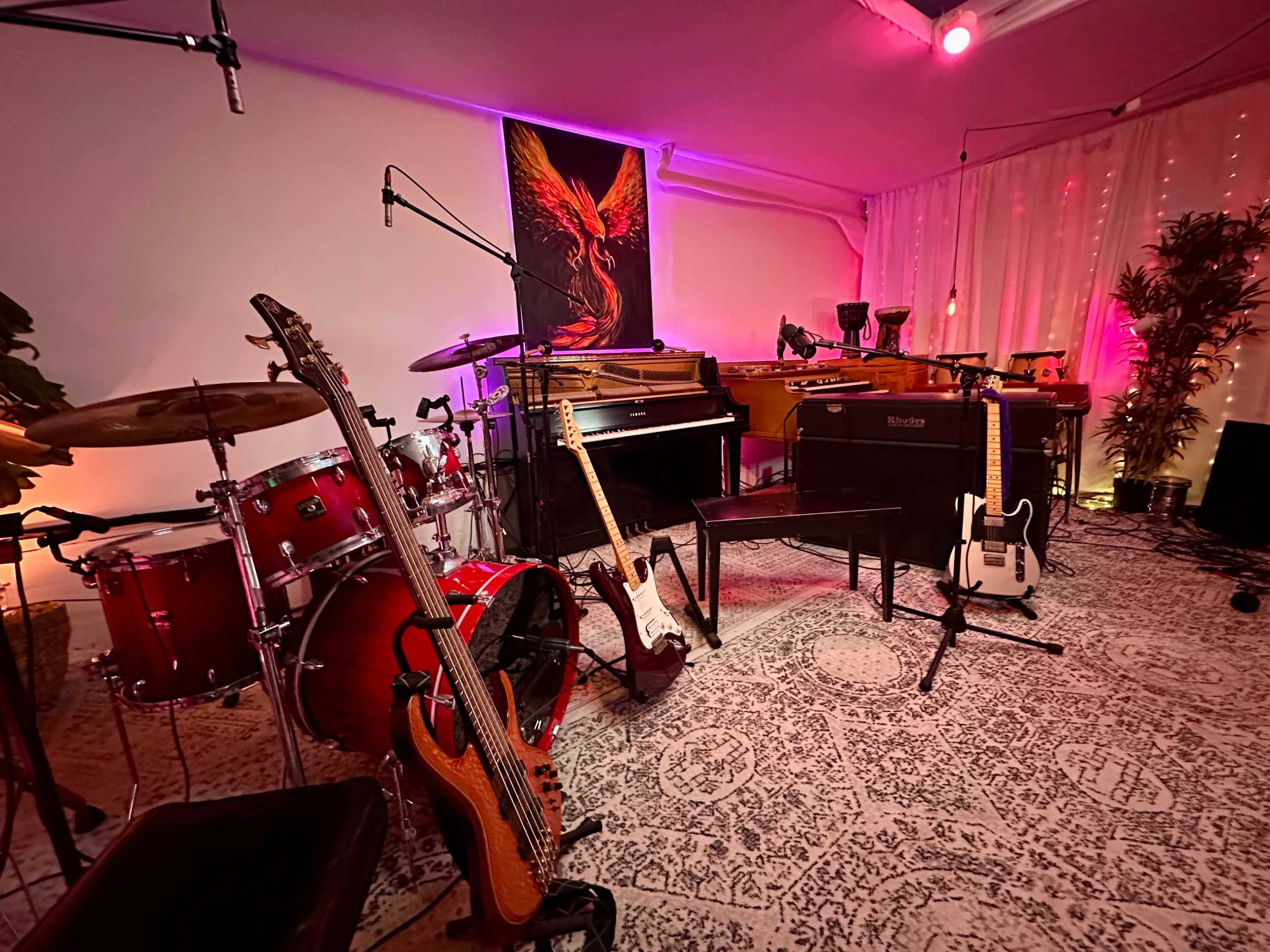 The image shows a music studio setup featuring various instruments, including a drum kit, acoustic and electric guitars, and a grand piano, with colorful lighting enhancing the ambiance.