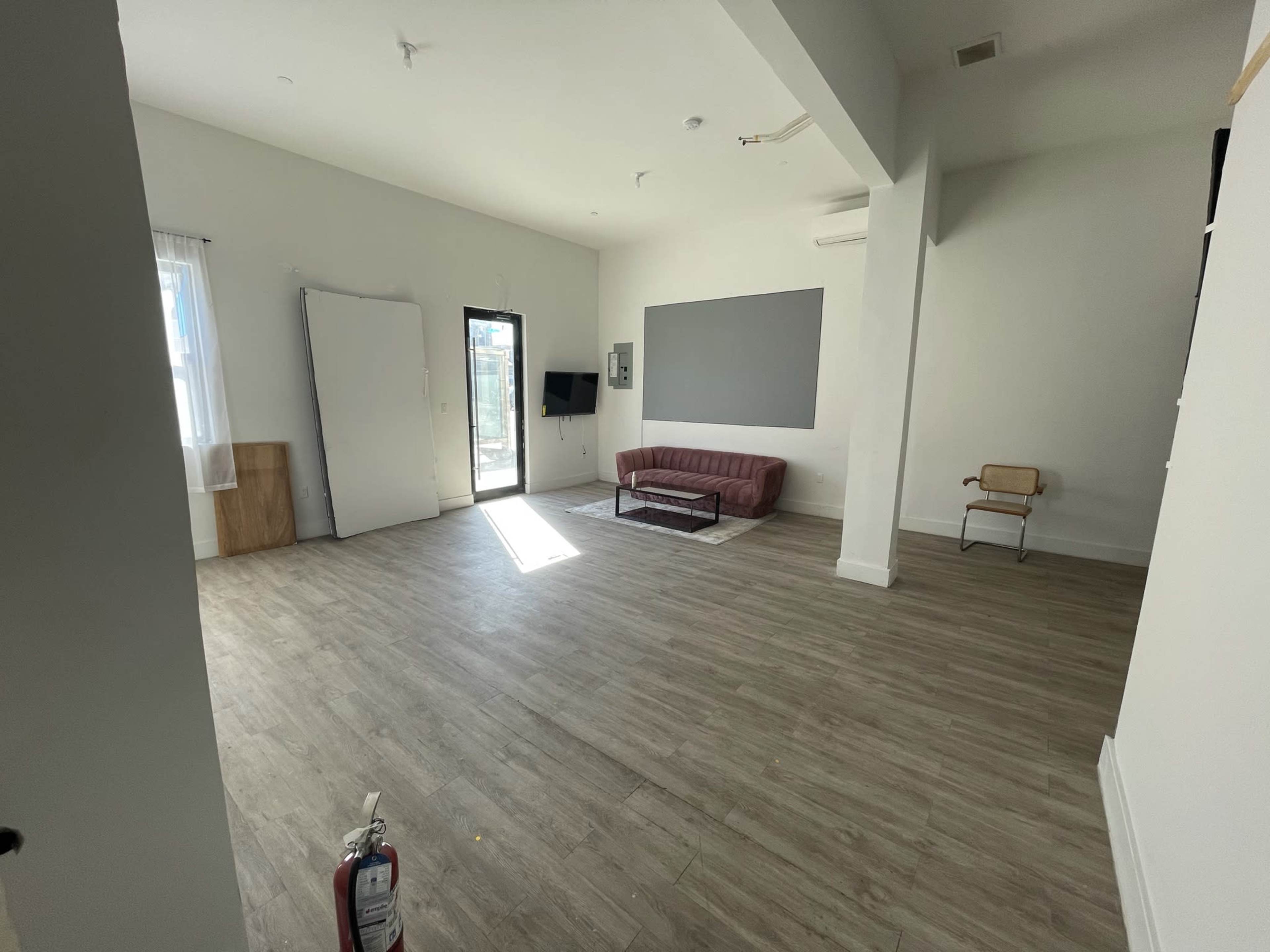 The room features a large, empty space with a couch, a television mounted on the wall, and a door leading to an outdoor area.