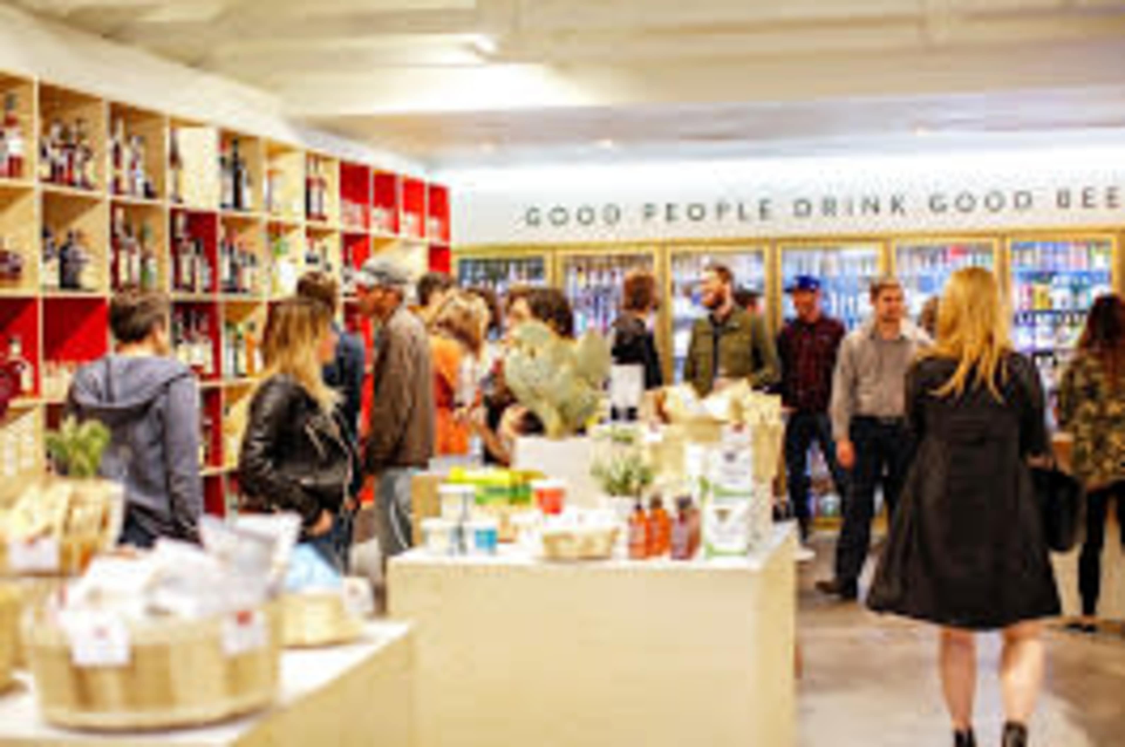A bustling store features shelves filled with a variety of beverages and products, while groups of people browse and socialize.