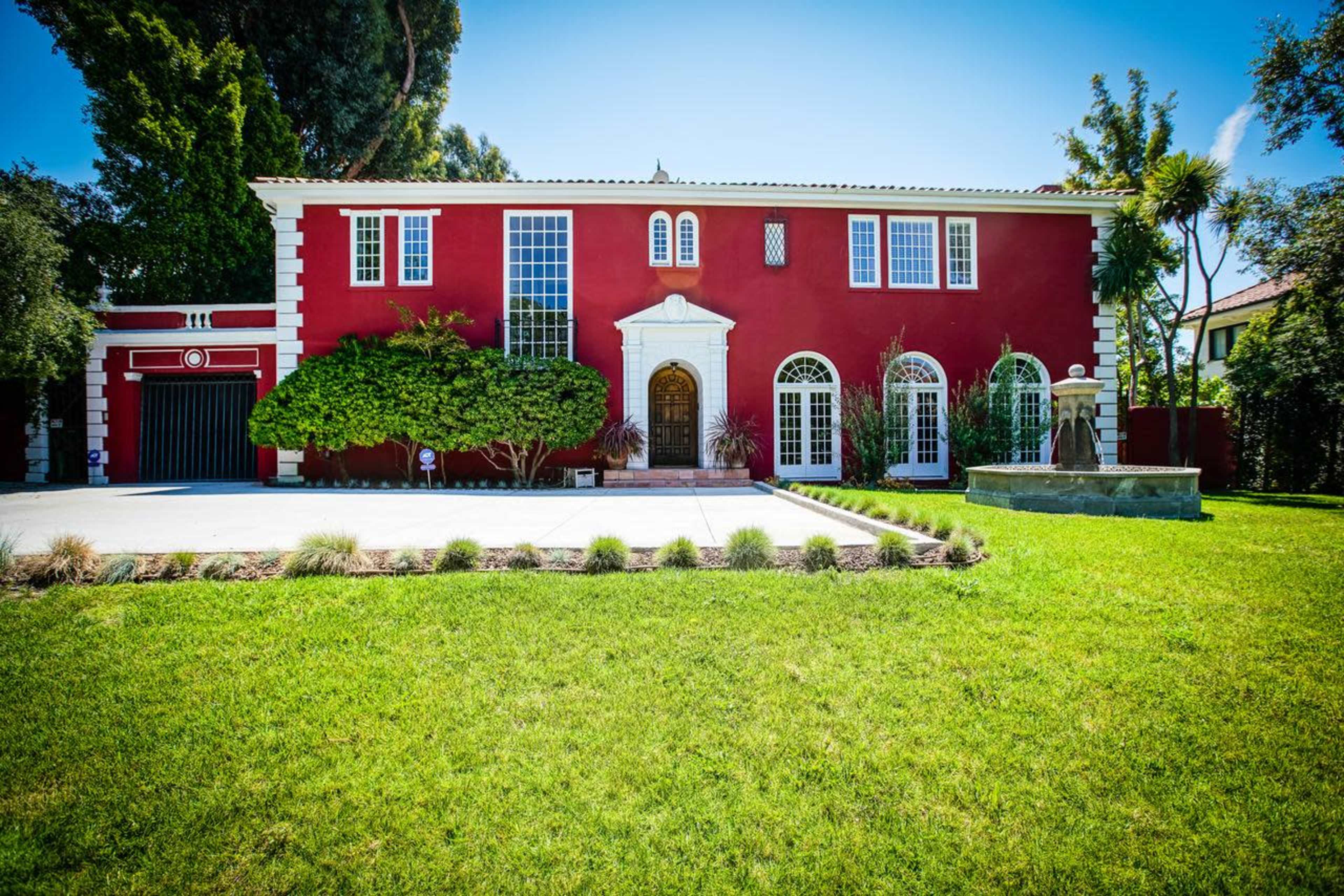 A red two-story house with a large front yard, decorative windows, and a manicured landscape.