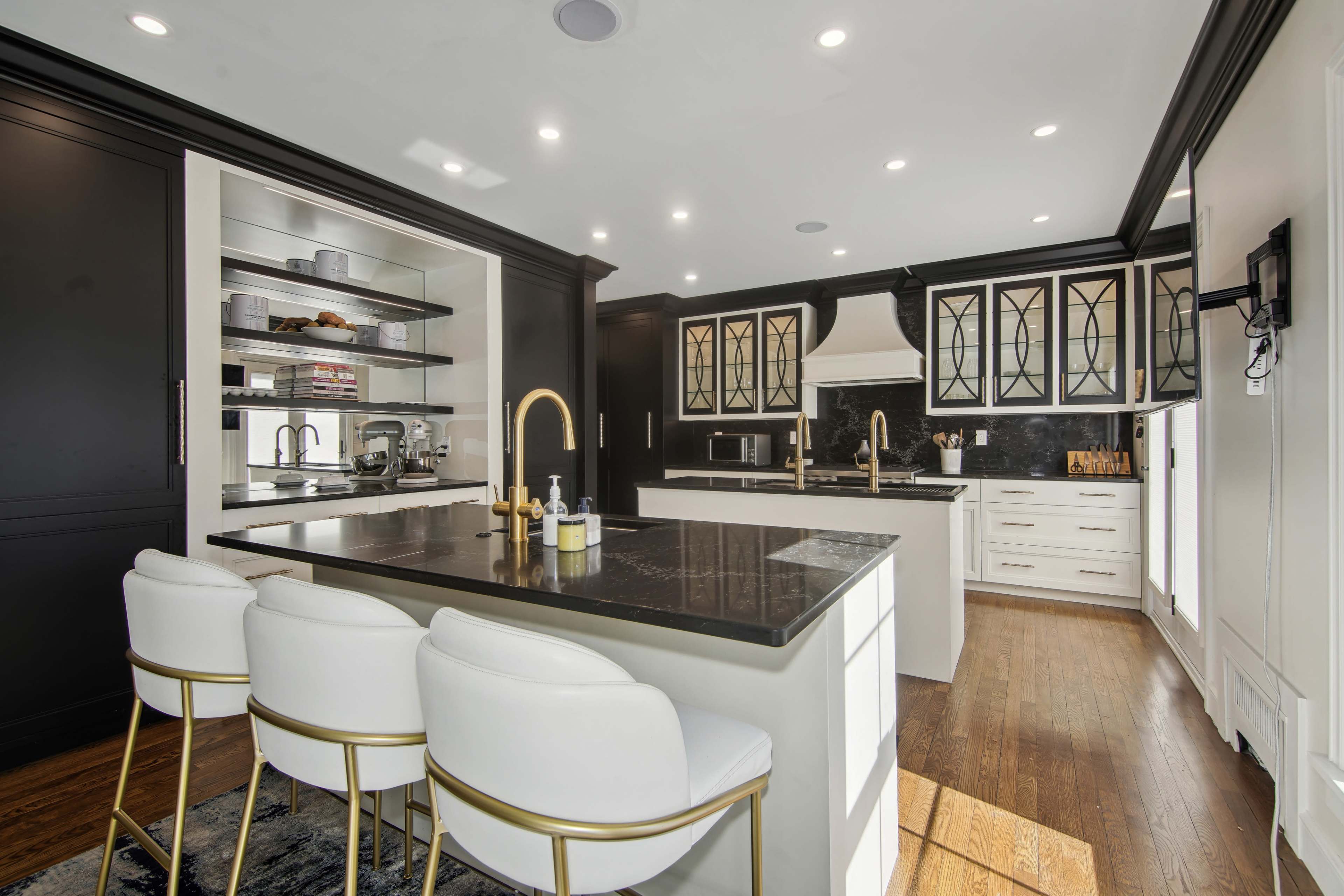 The kitchen features black cabinetry, a central island with white bar stools, and modern appliances against a contrasting black backsplash.