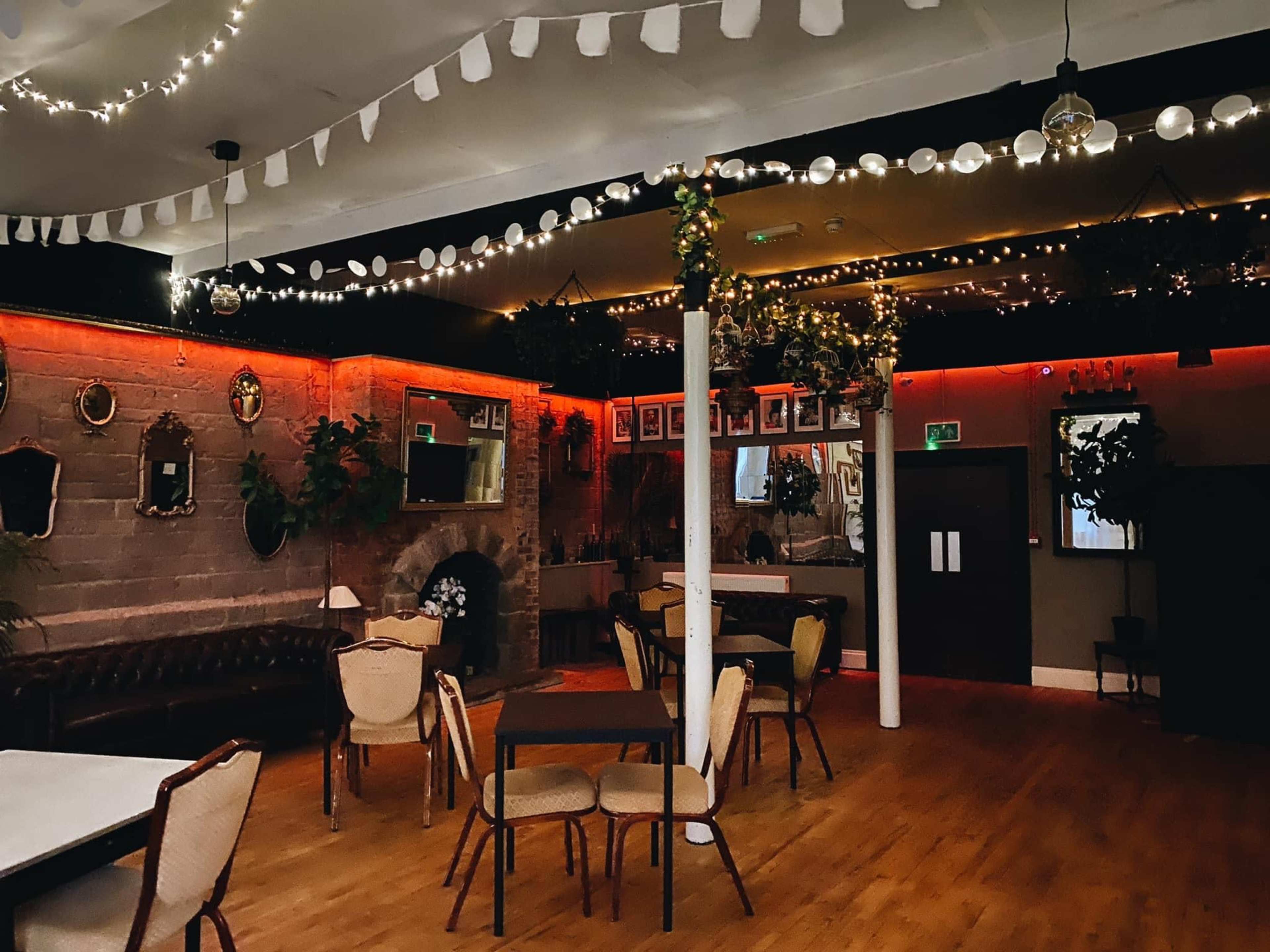 A well-lit event space featuring a mix of seating arrangements, decorative plants, and string lights.