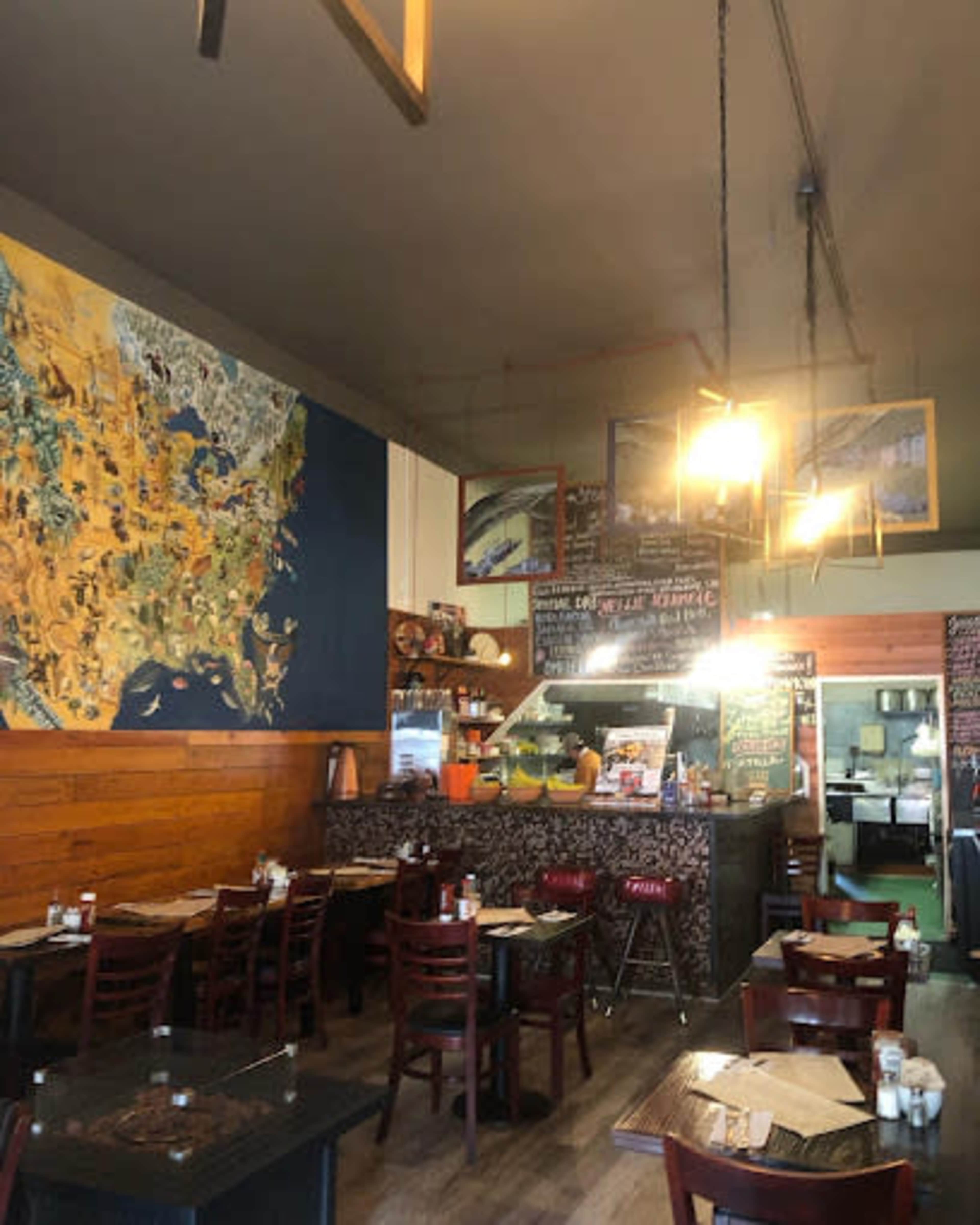 The image shows the interior of a restaurant featuring wooden walls, tables set for dining, and a large mural of a map on one wall.