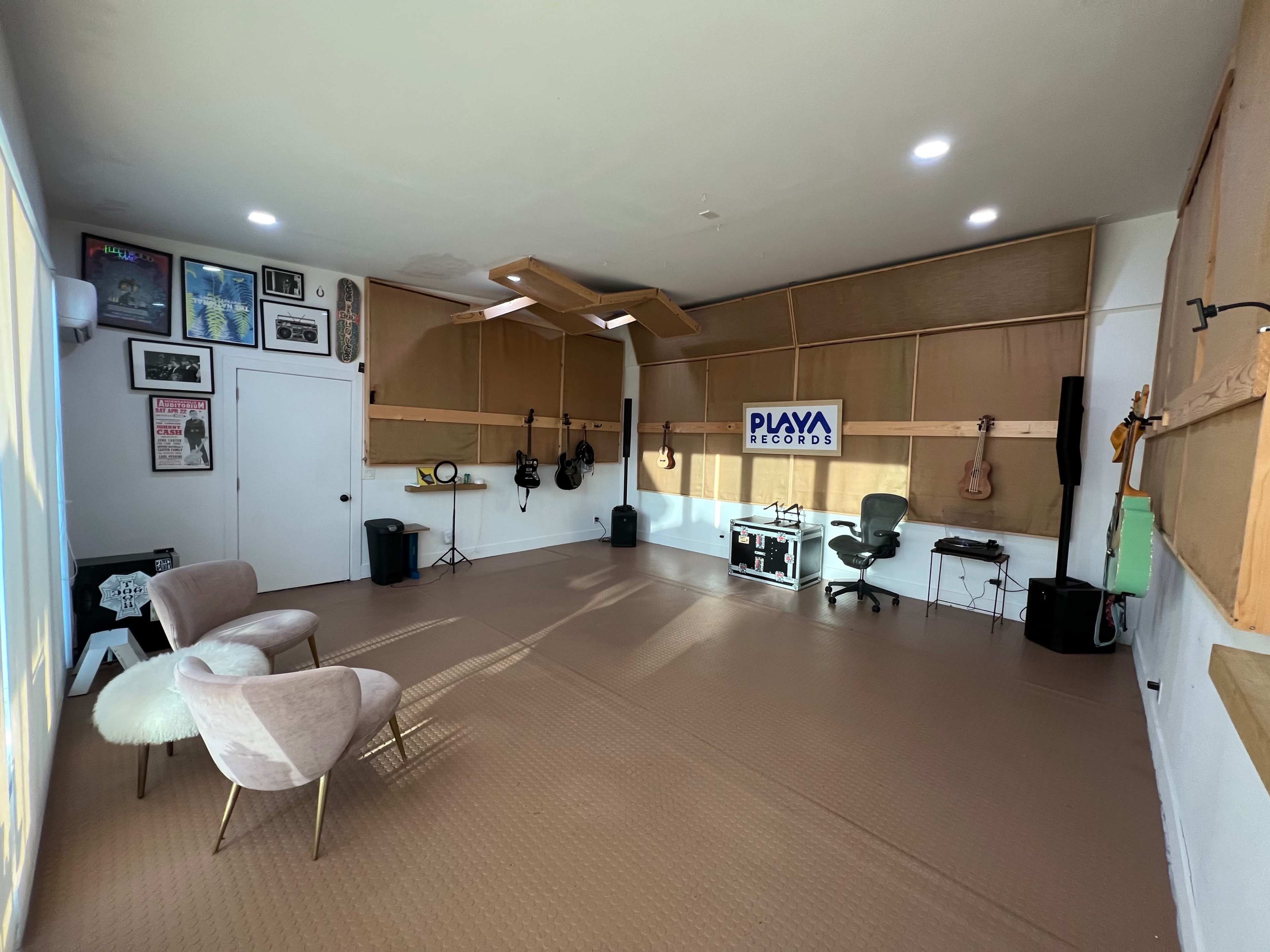 The image shows a spacious recording studio featuring a minimalist design with guitars on the walls and seating in one corner.