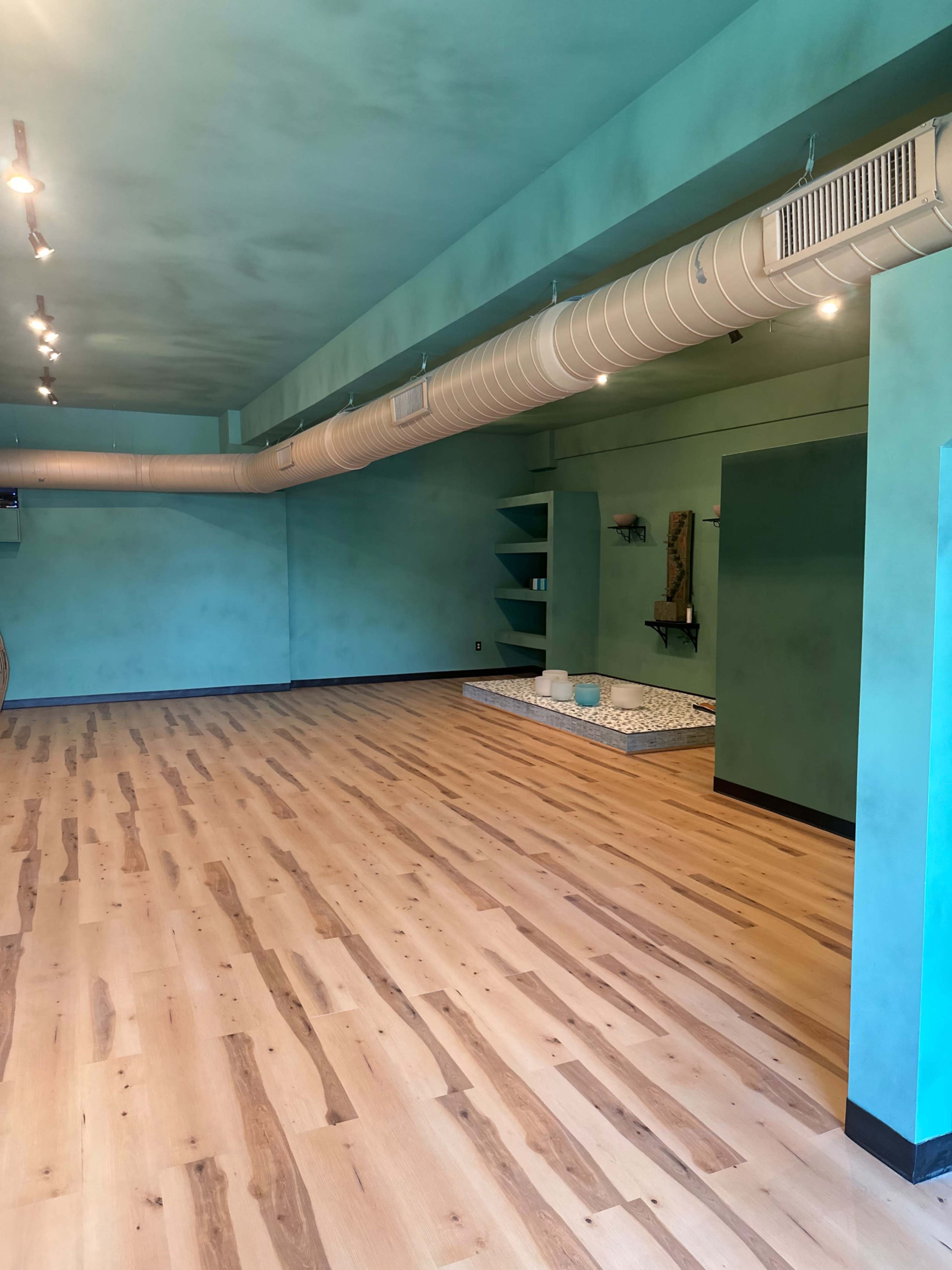 A spacious room with light wood flooring, teal walls, and a cozy area with cushions on the floor.